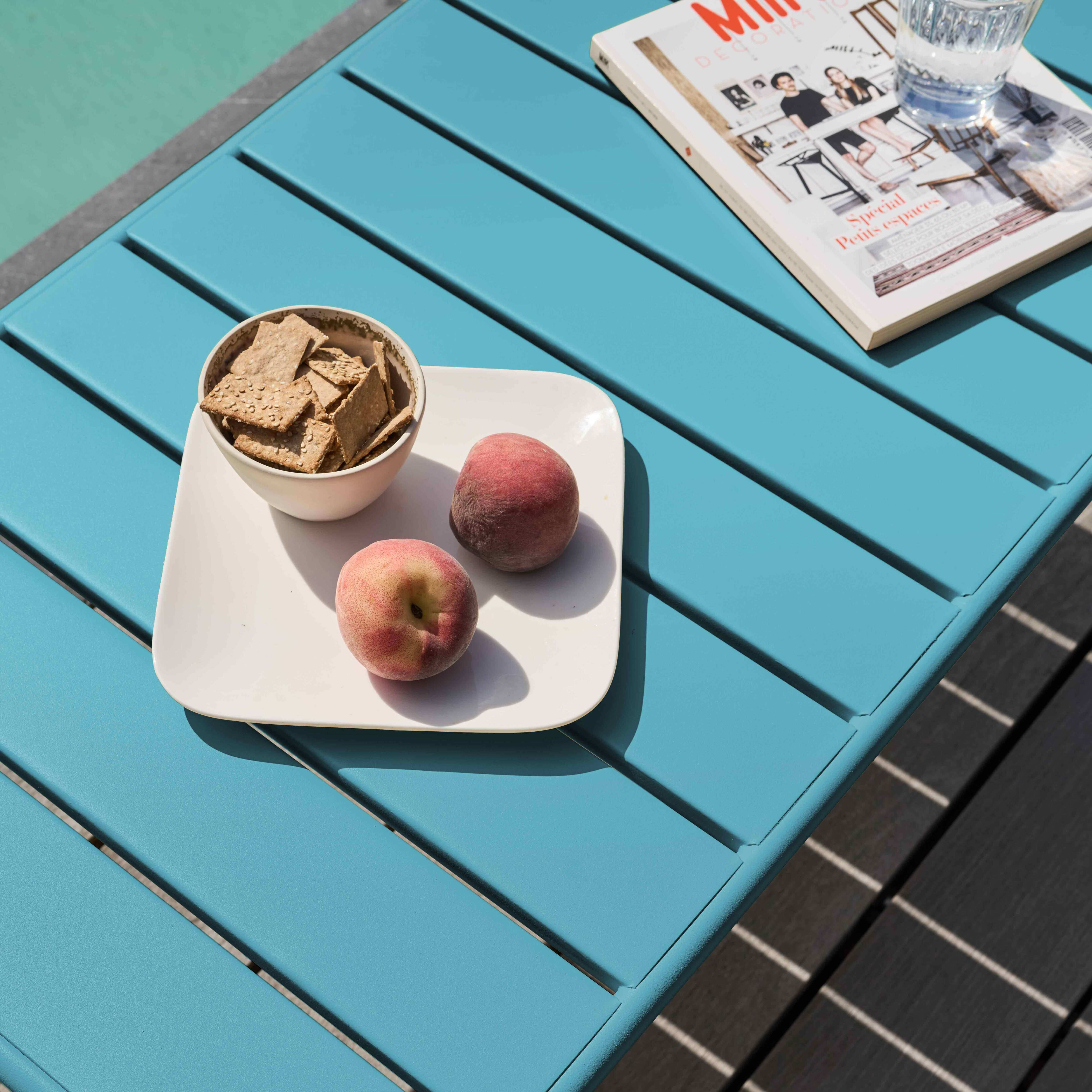 Ein blauer Tisch mit Essen und einer Zeitschrift. Auf dem Tisch liegen Pfirsiche, Cracker und ein Glas Wasser.