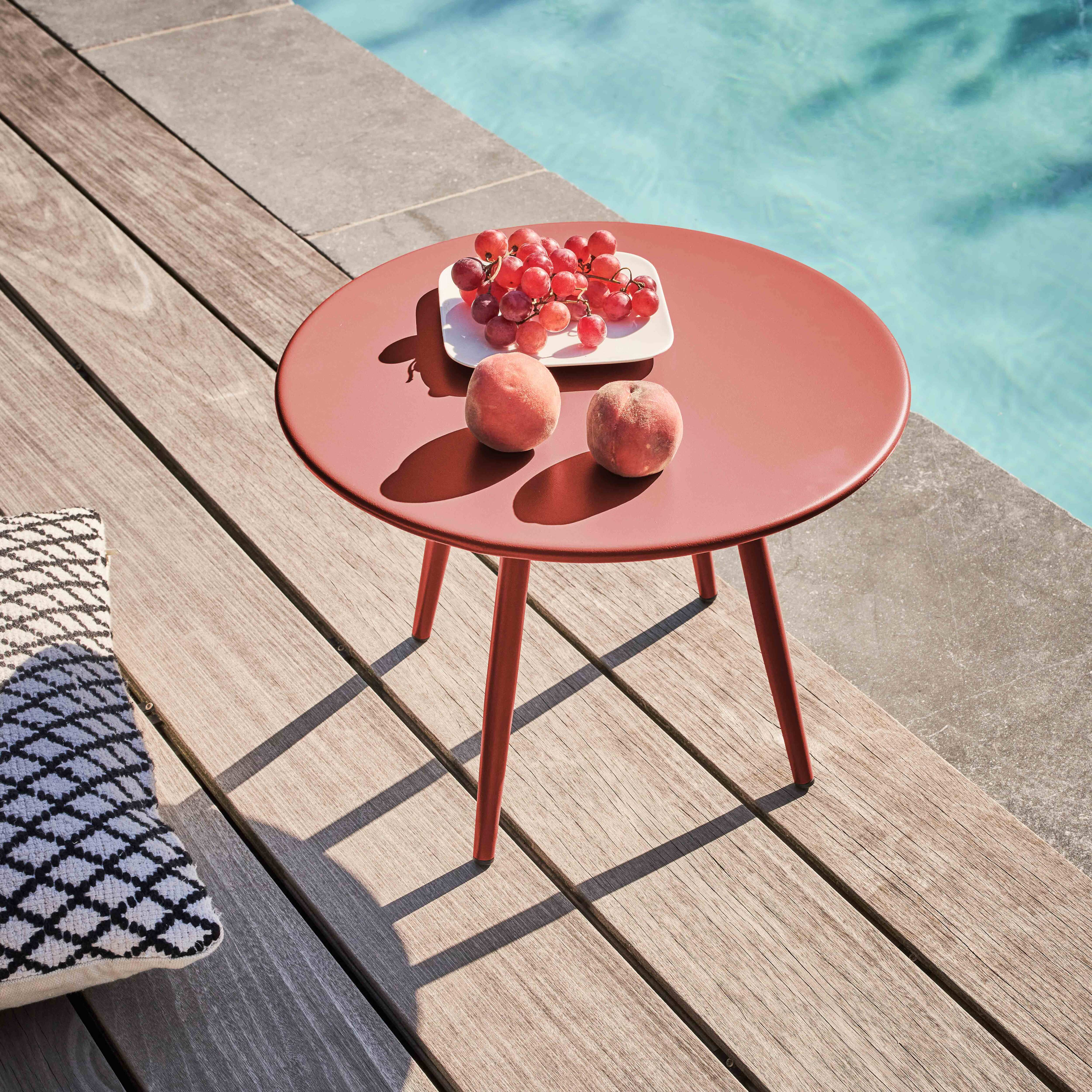 Ein roter Tisch mit Trauben und Pfirsichen steht auf einer Holzterrasse am Pool. Links liegt ein Kissen.