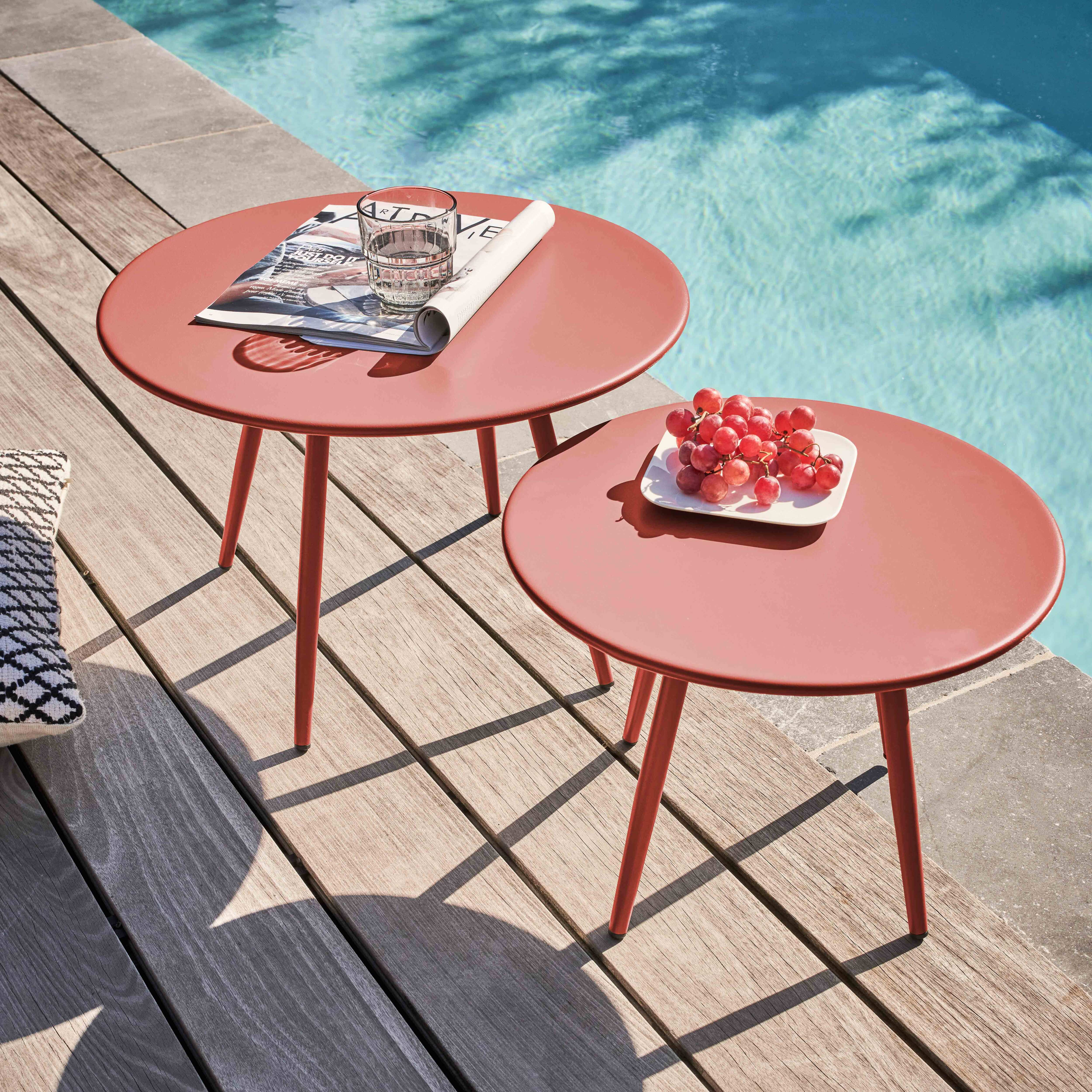 Zwei korallenfarbene Tische mit Trauben und einem Glas stehen auf einem Holzdeck neben einem Pool.