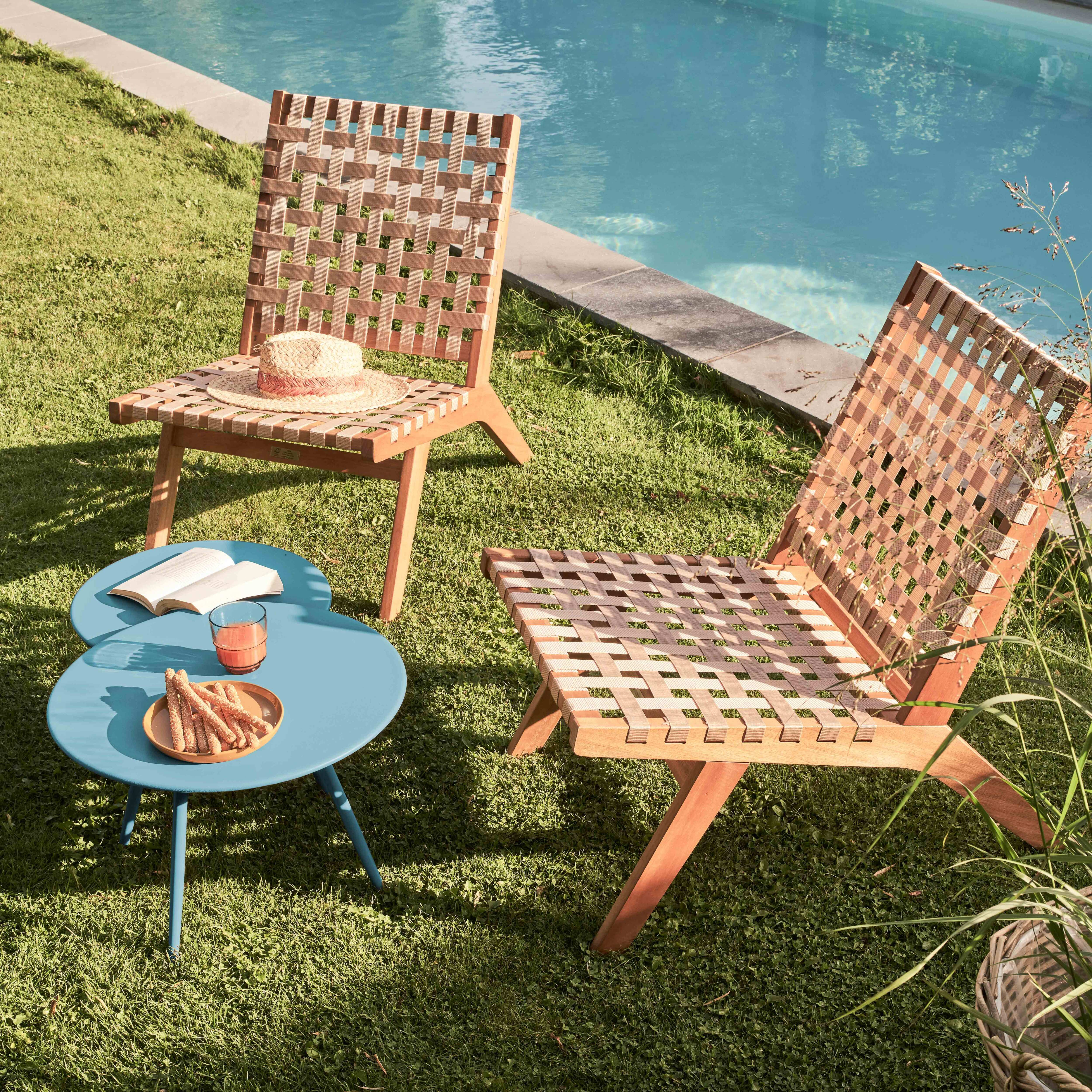 Zwei Stühle und ein Tisch stehen in einem Garten in der Nähe eines Pools. Auf einem Stuhl liegt ein Hut. Auf dem Tisch Snacks und Getränke.