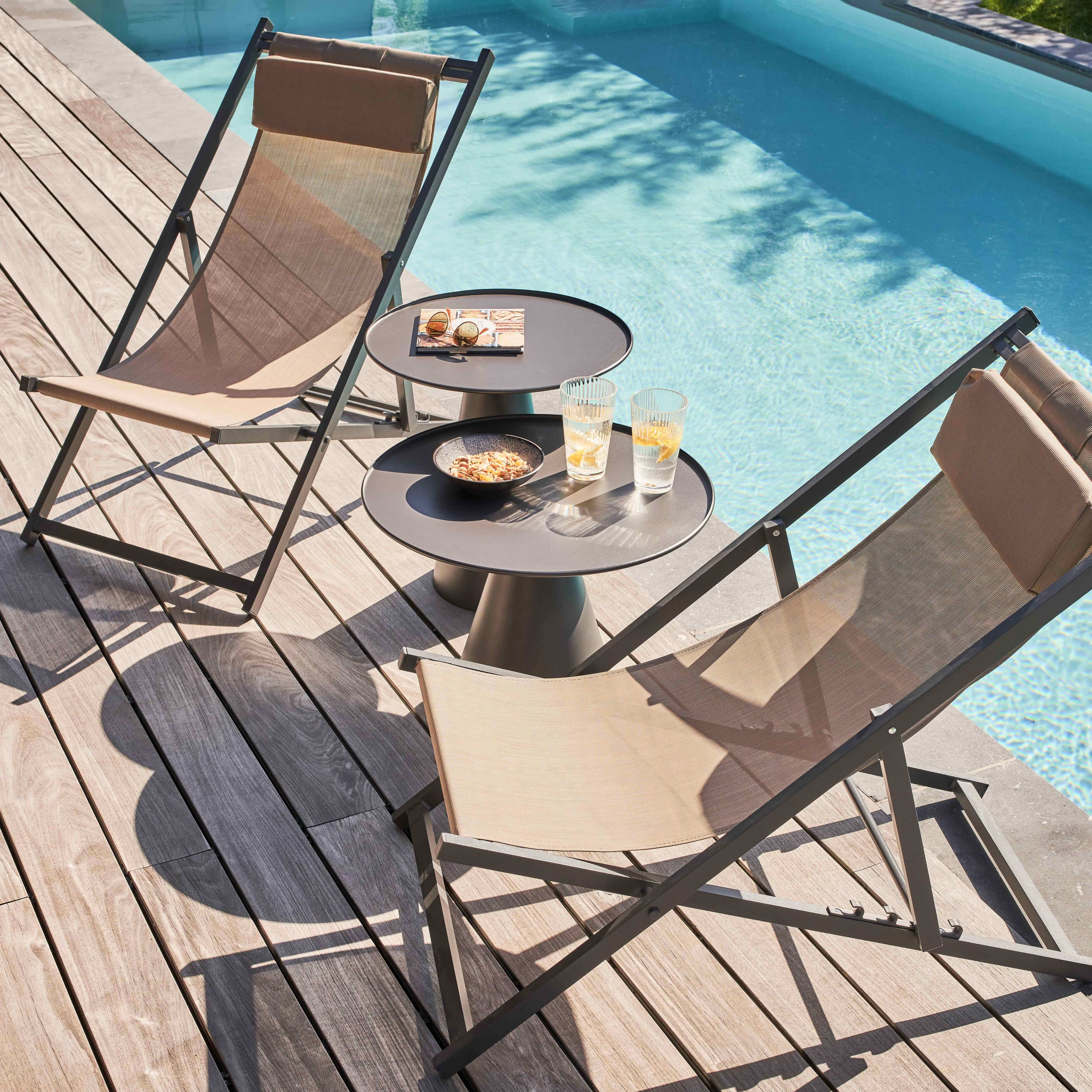 Zwei beige Liegestühle am Pool. Tische mit Snacks und Getränken stehen dazwischen. Holzterrasse.