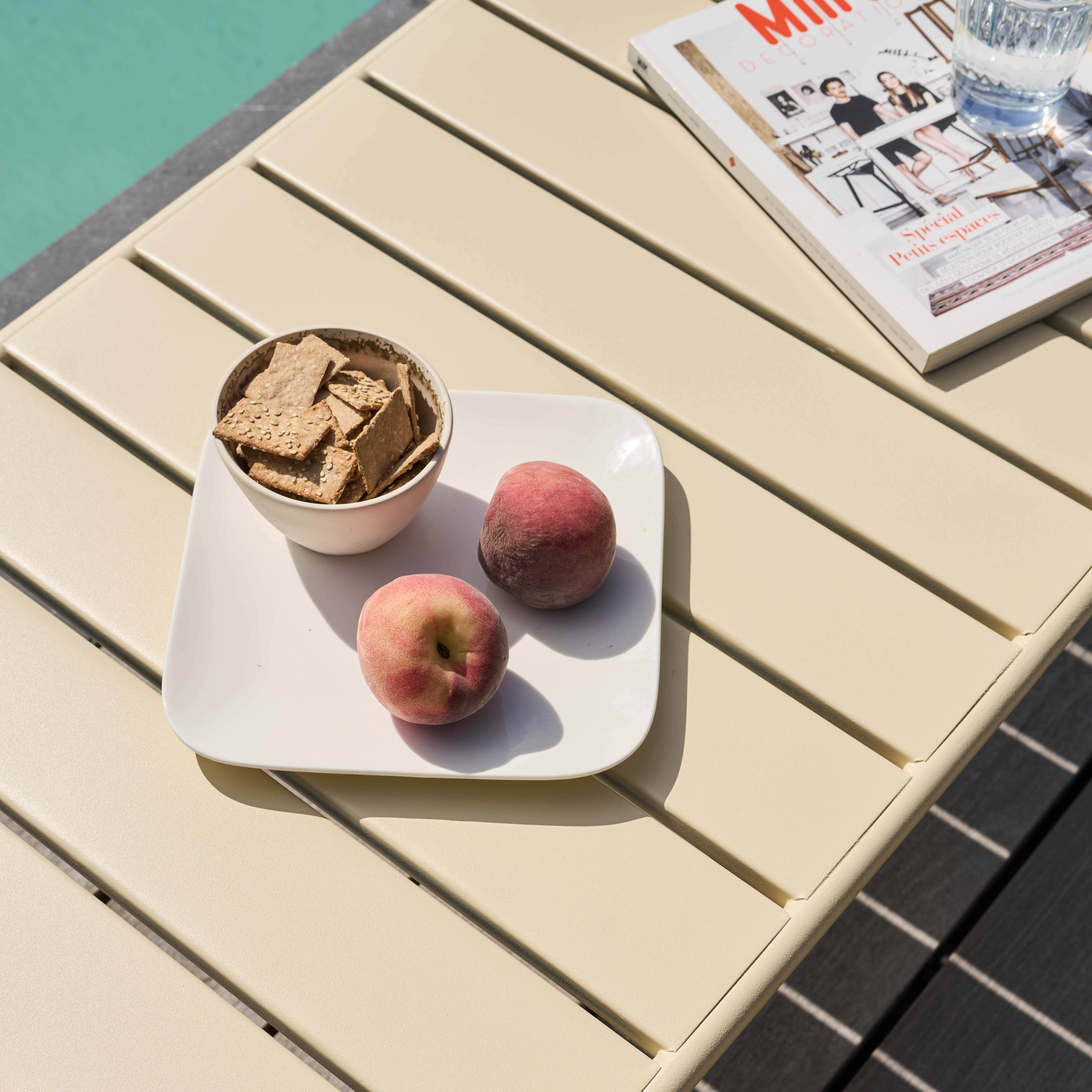 Ein Tisch mit Crackern, Pfirsichen und einer Zeitschrift neben einem Pool. Der Tisch ist beige.