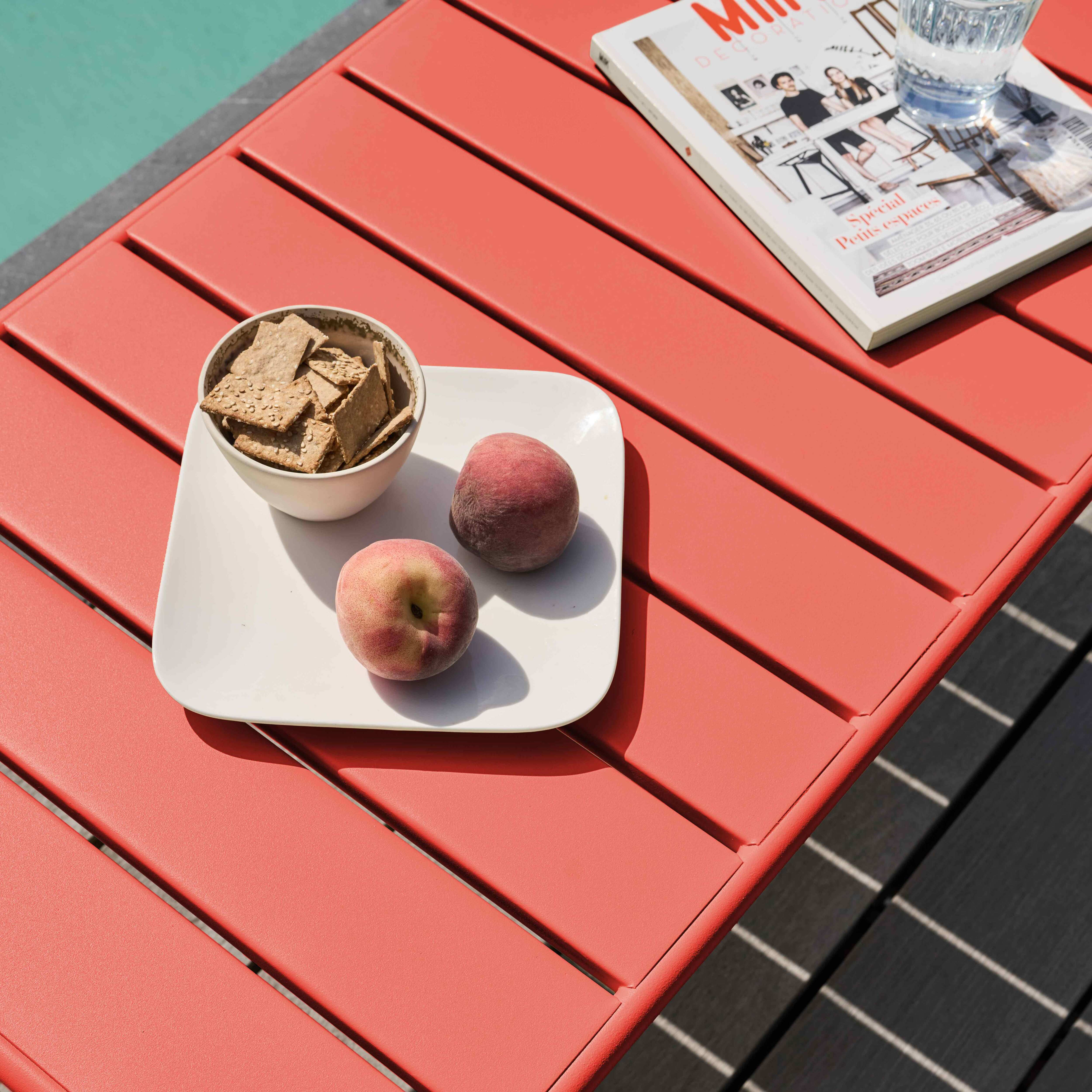Ein roter Tisch mit Snacks und Pfirsichen, einer Zeitschrift und einem Glas Wasser. Der Hintergrund ist ein Pool.