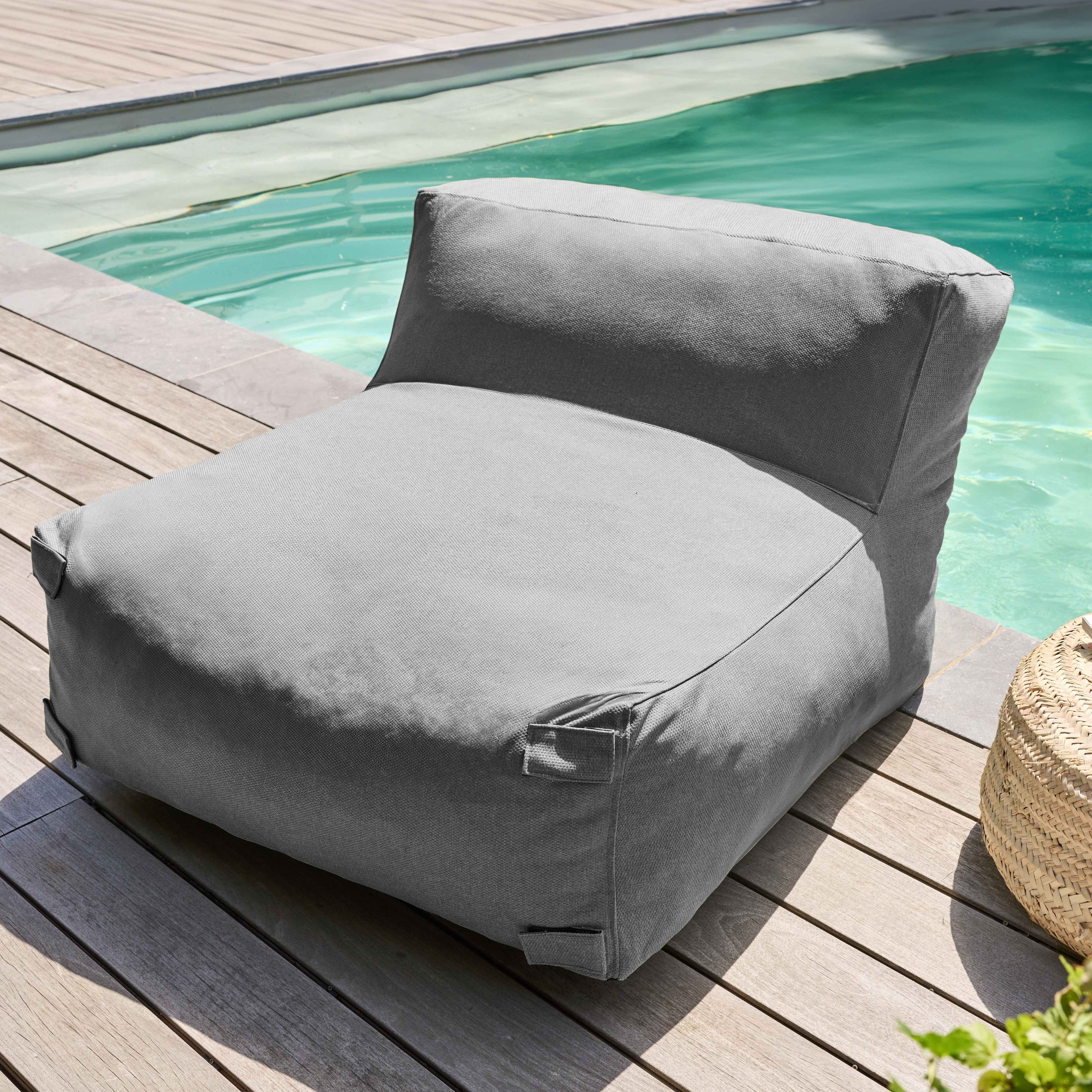 Ein grauer Sitzsack steht auf Holzplanken am Pool. Ein gewebter Korb und Grünzeug befinden sich in der Nähe.