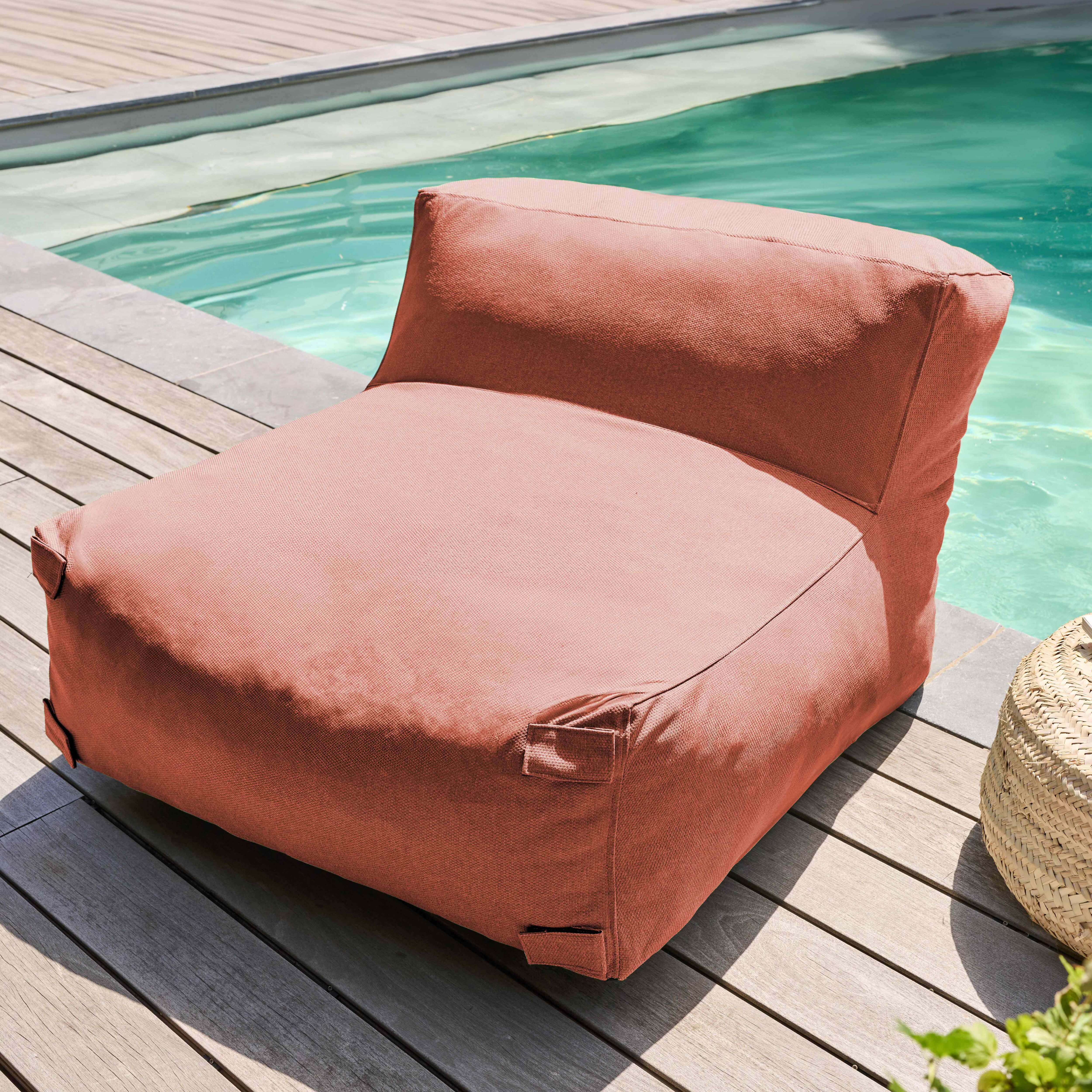 Ein korallenfarbener Sitzsackstuhl steht auf Holzdecks neben einem Pool. Ein geflochtener Korb und Laub sind ebenfalls sichtbar.