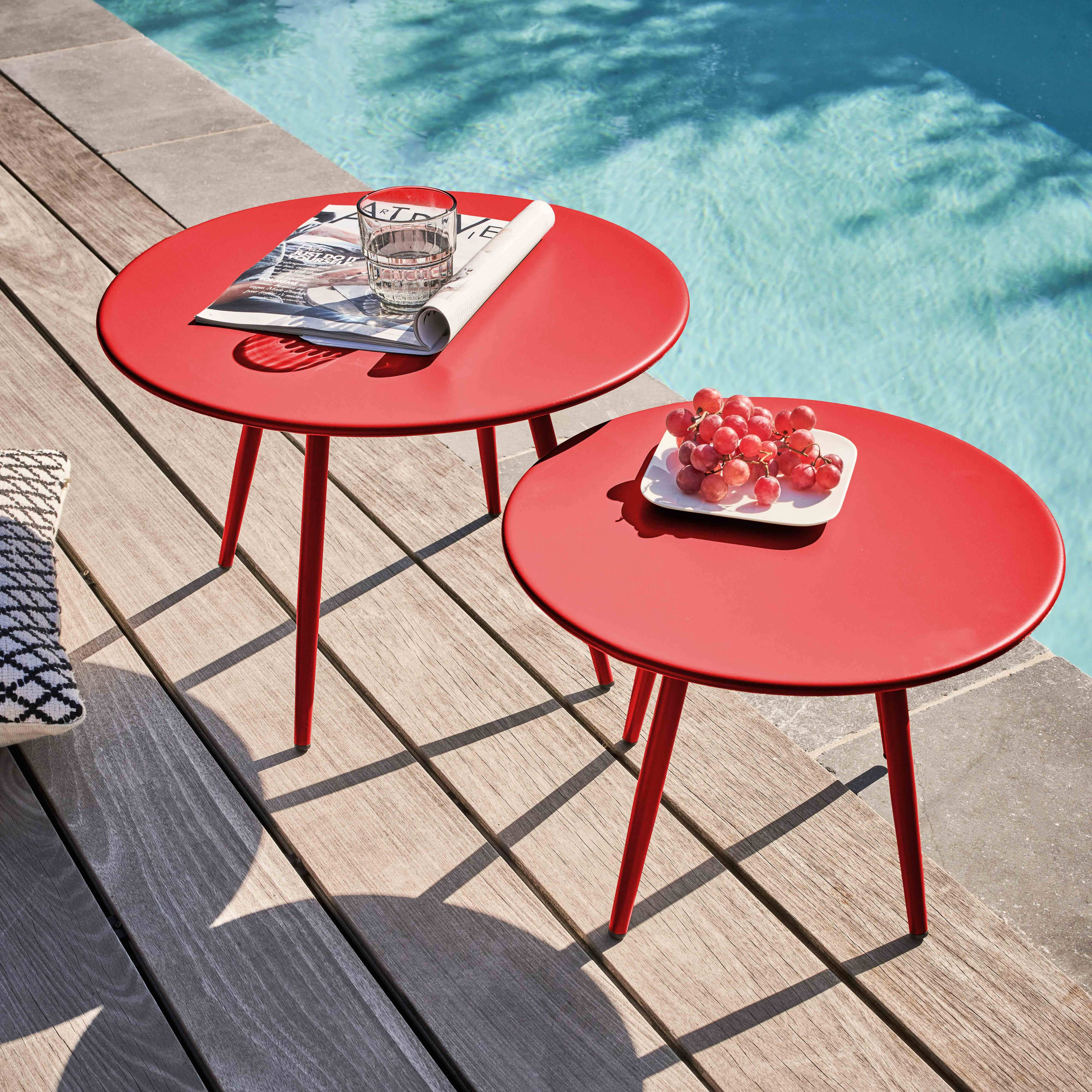 Zwei rote Tische mit Gegenständen auf einem Holzdeck neben einem Pool. Trauben auf dem einen, ein Glas und eine Zeitschrift auf dem anderen.
