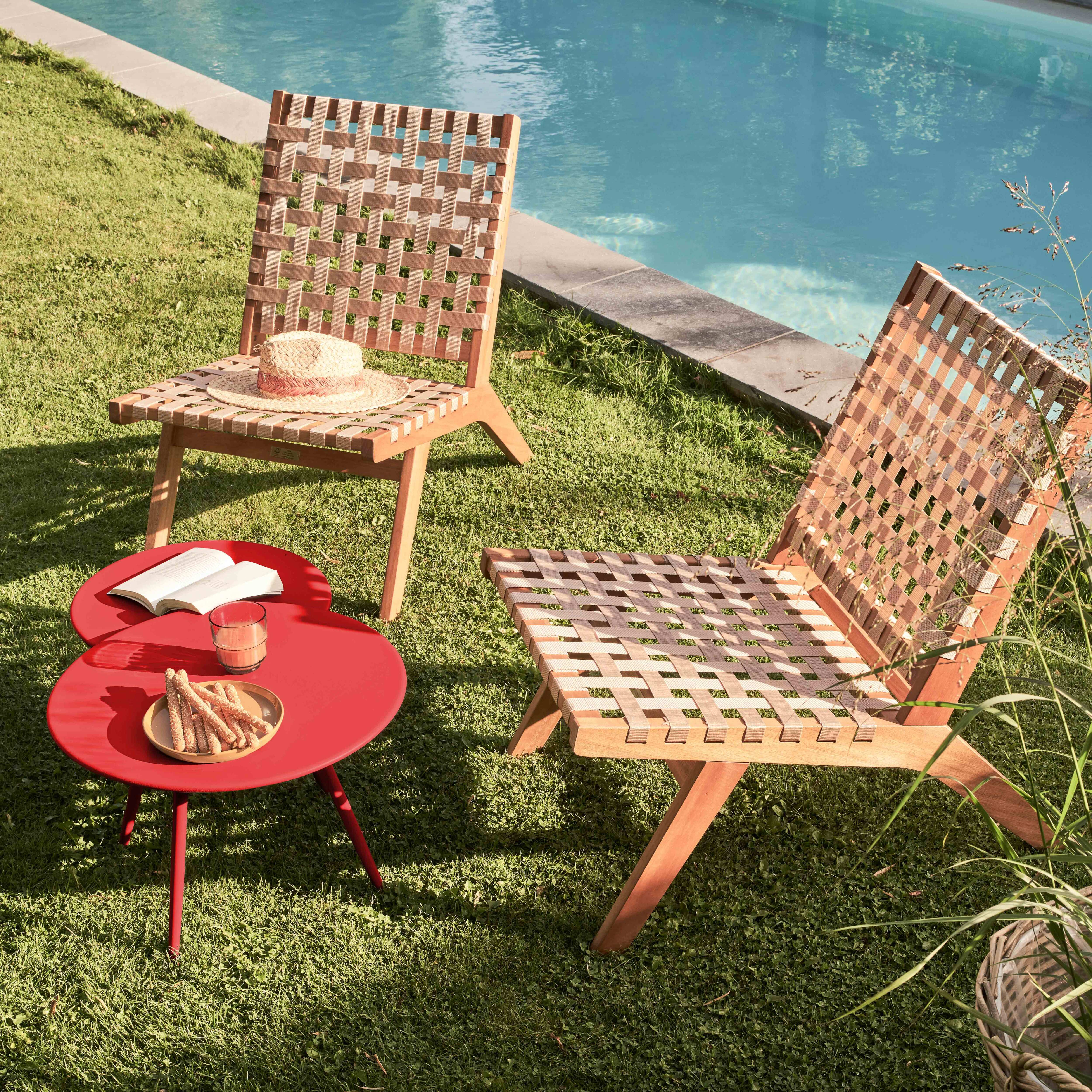 Zwei Stühle, ein roter Tisch mit Snacks, ein Pool und ein Strohhut auf dem Stuhl. Die Szene spielt auf einer grünen Wiese.