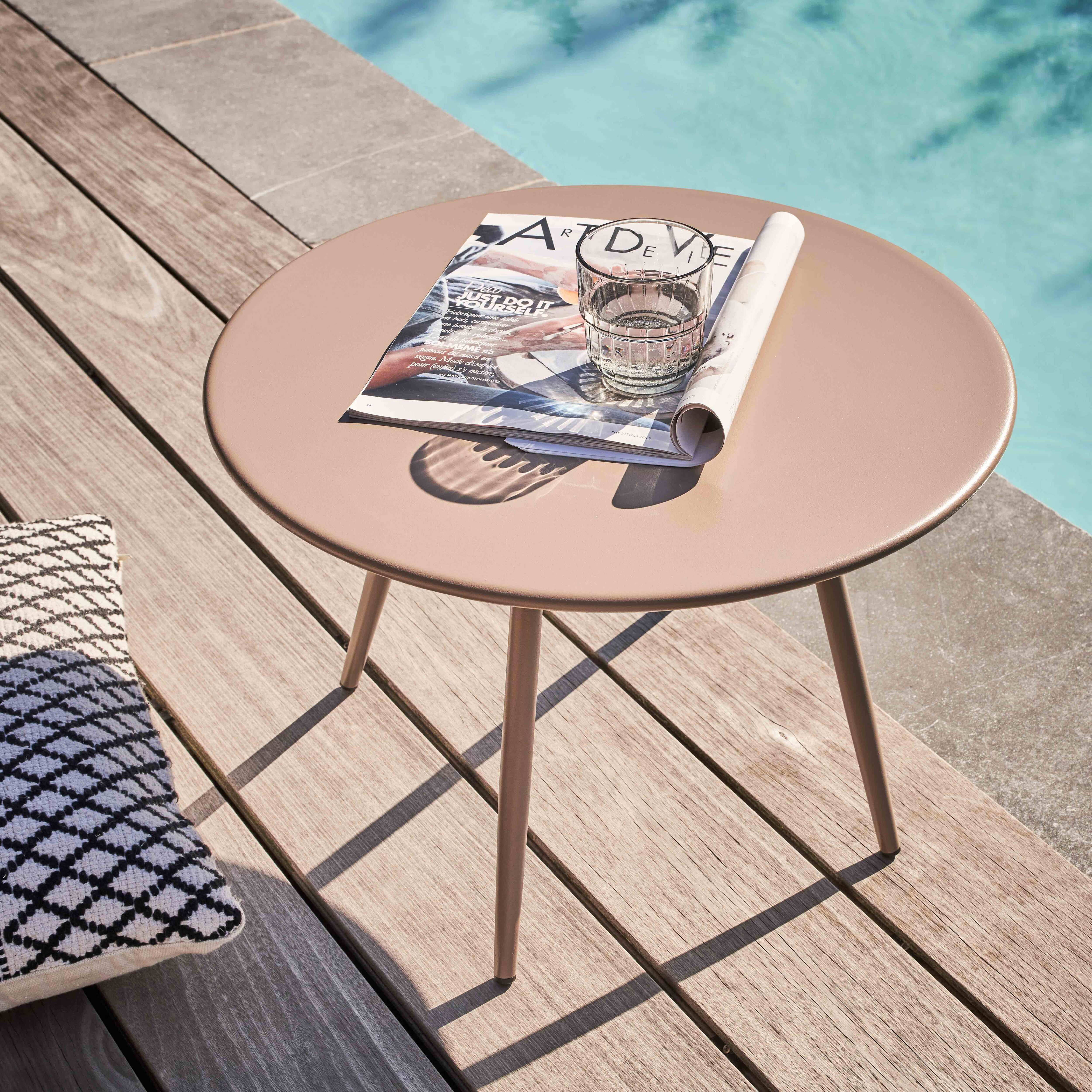 Ein runder Tisch mit einer Zeitschrift und einem Wasserglas. Ein Kissen und Pool im Hintergrund.