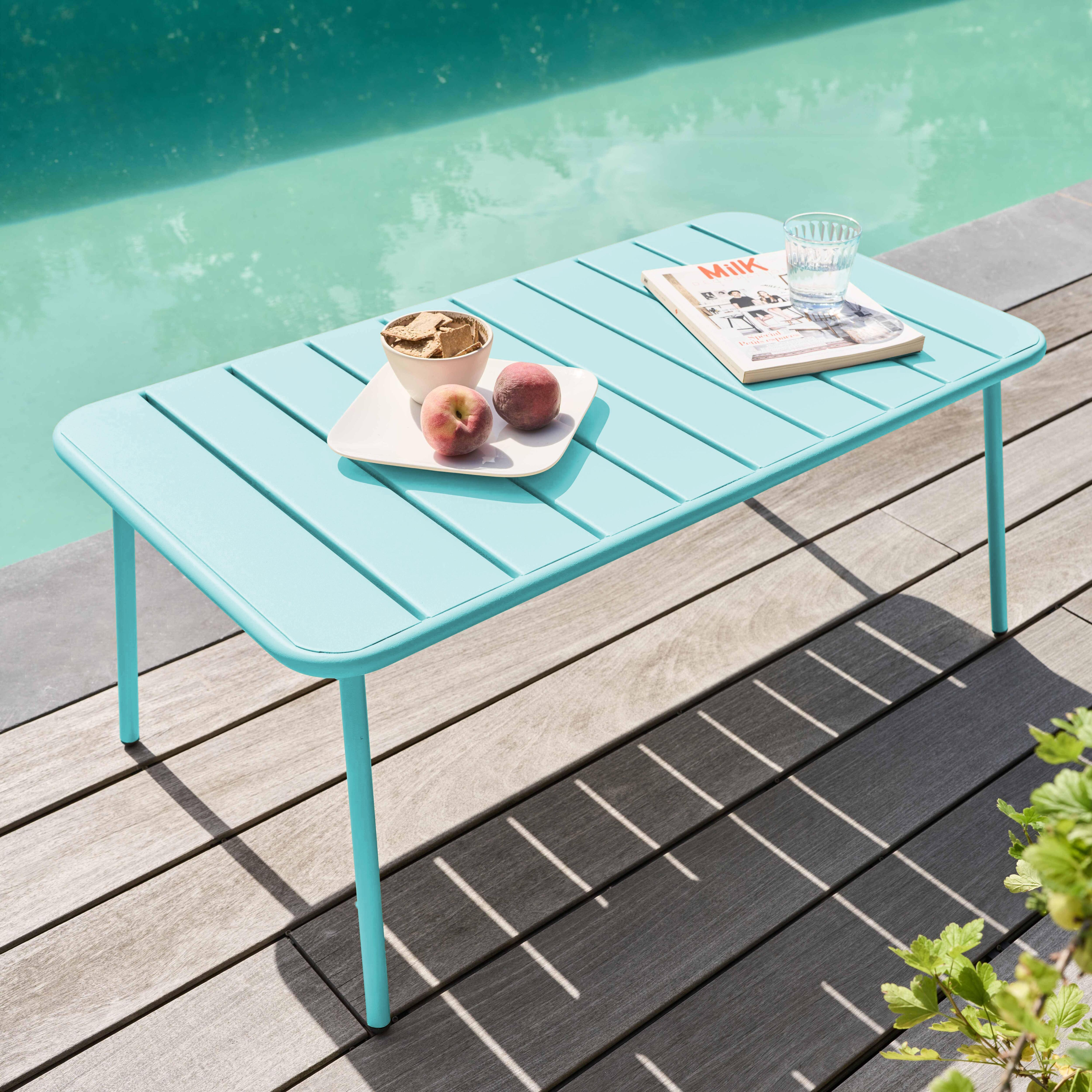 Ein blauer Tisch mit Snacks und Obst steht am Pool. Ein Glas Wasser und eine Zeitschrift liegen auf dem Tisch.
