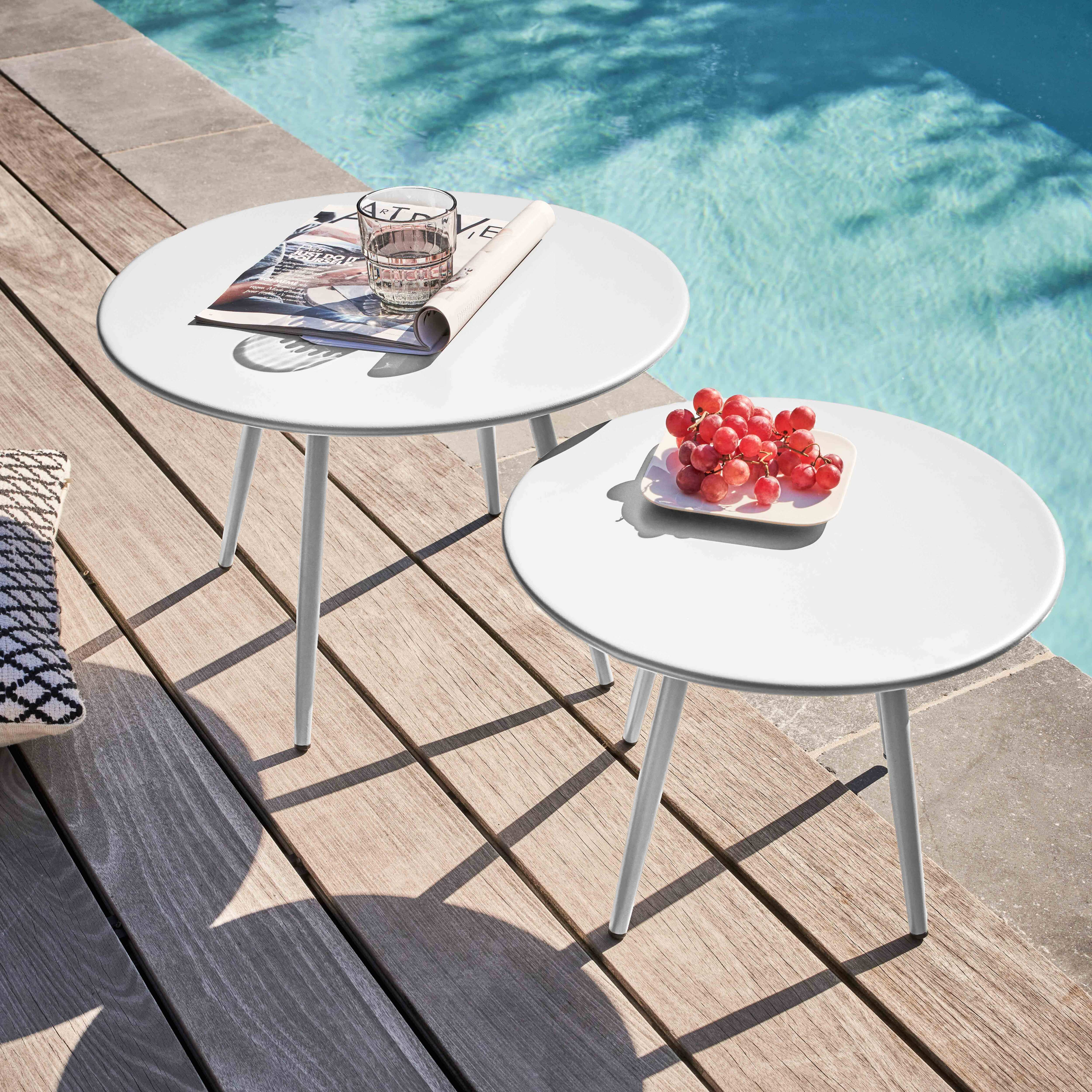 Zwei weiße Tische mit Getränken und Obst auf einem Holzdeck neben einem Pool. Schatten werden geworfen.