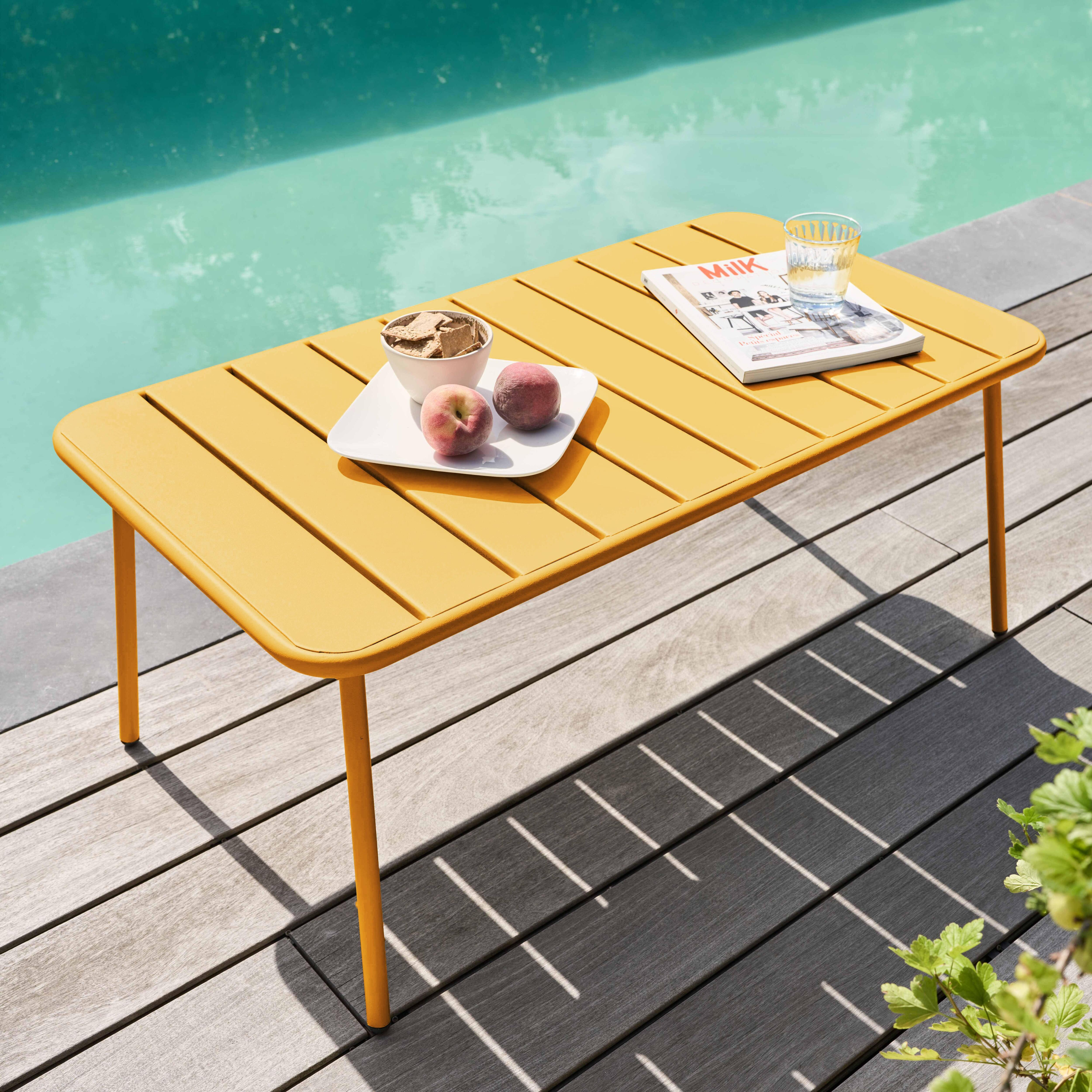 Ein gelber Tisch mit Essen und einem Glas Wasser steht am Pool. Pfirsiche, Cracker und eine Zeitschrift liegen auf dem Tisch.