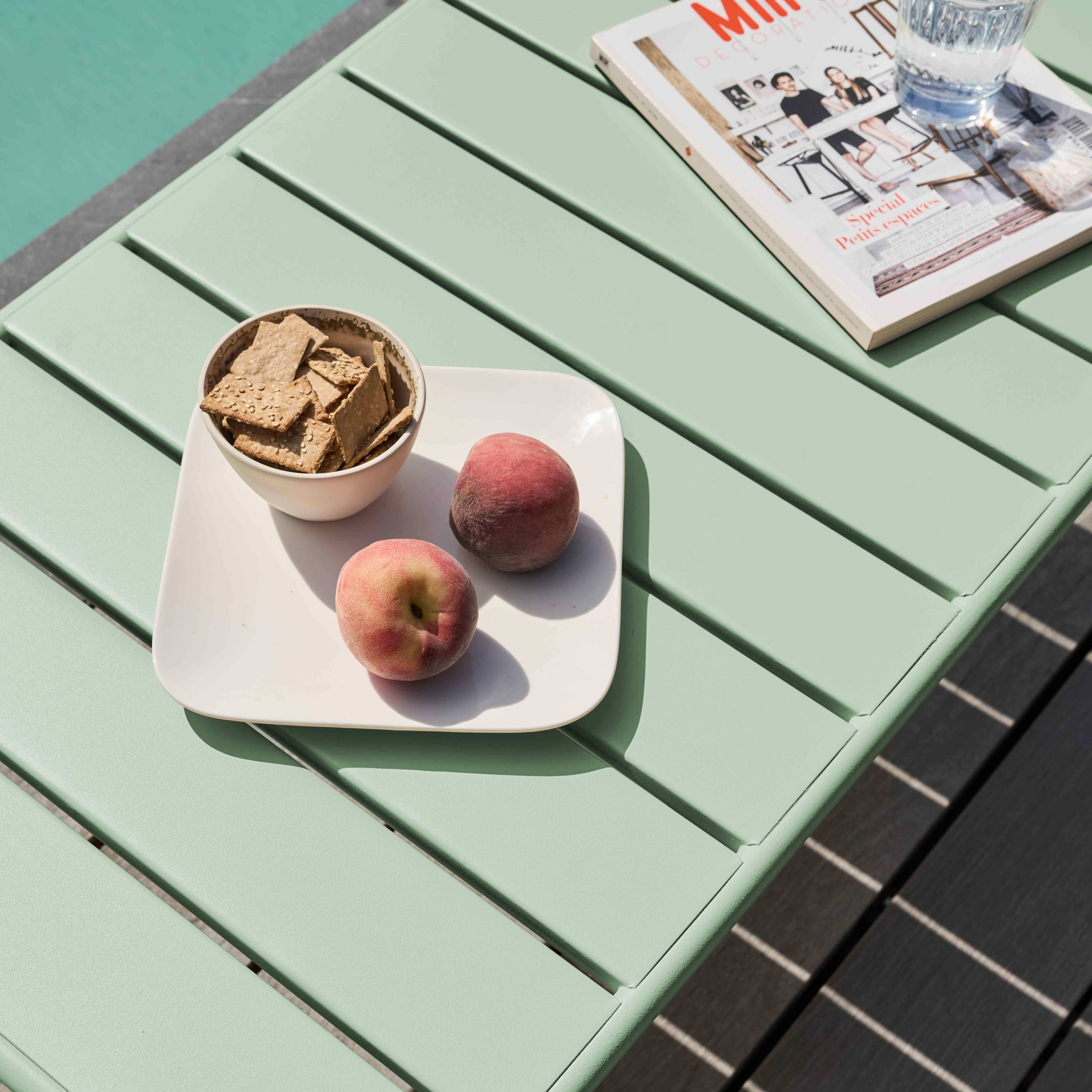 Tisch mit Obst, Crackern und einer Zeitschrift. Ein Glas Wasser ist ebenfalls vorhanden. Der Tisch ist hellgrün.