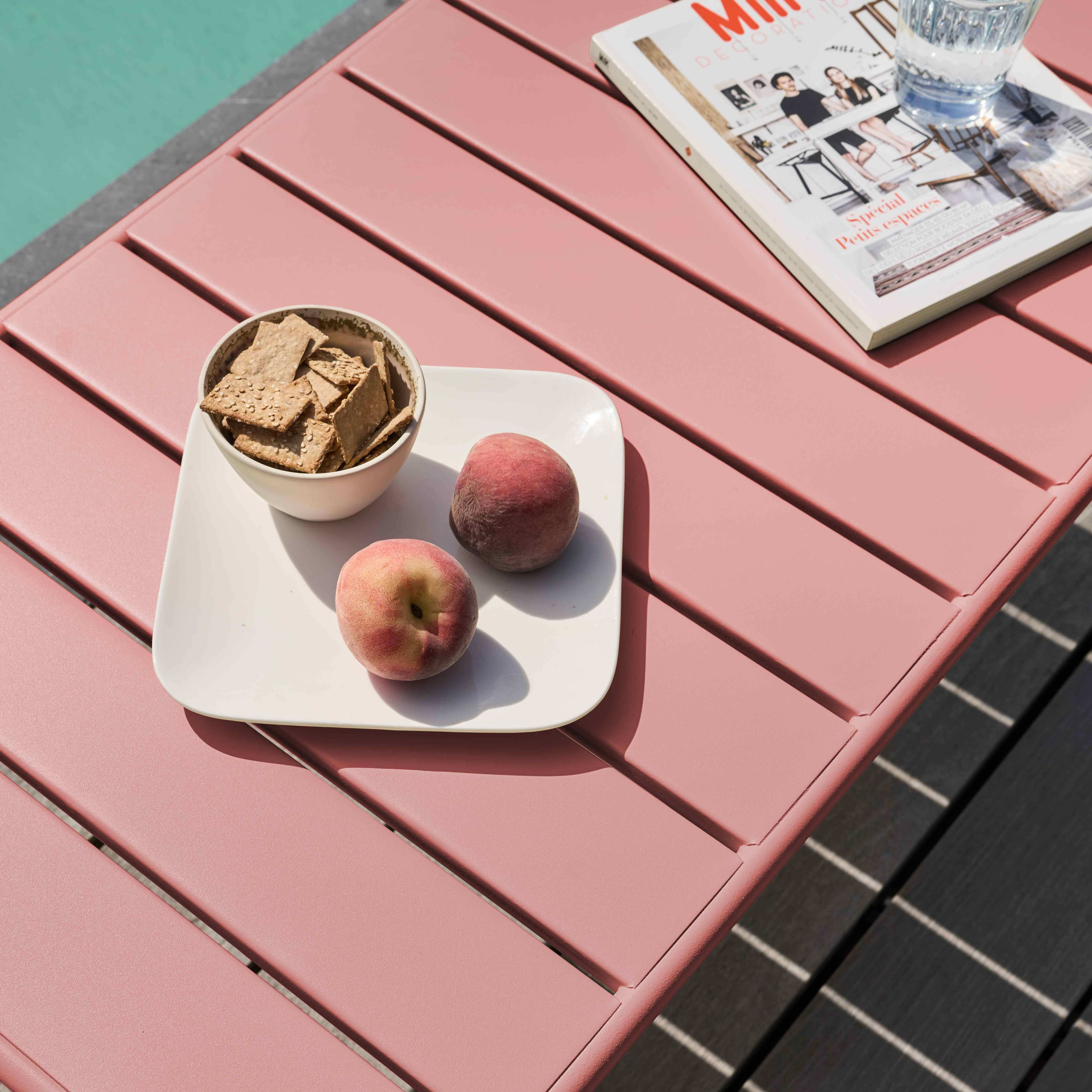 Rosa Tisch mit Snacks, Pfirsichen, Zeitschrift und Wasserglas. Pool im Hintergrund.