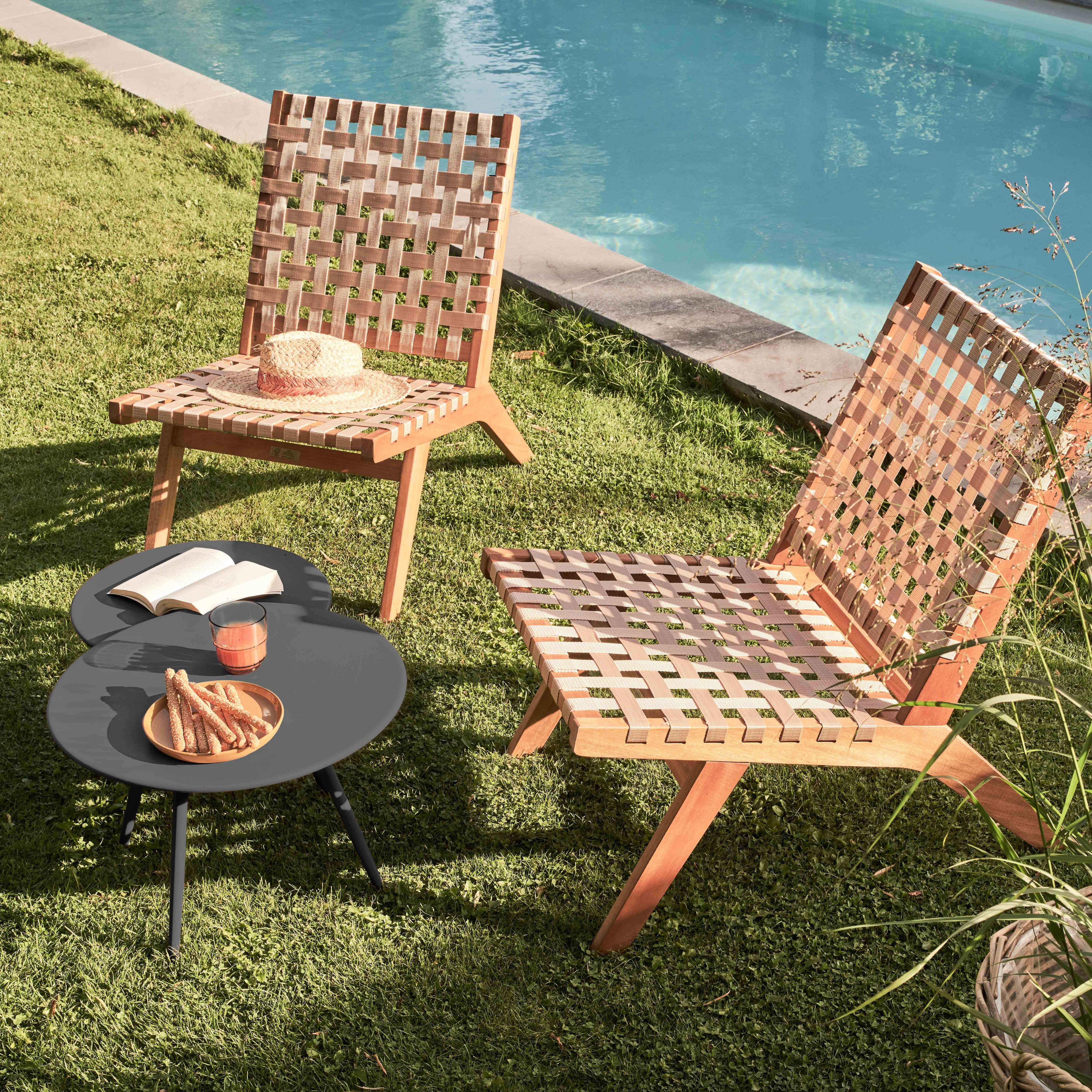 Außenszene mit zwei Holzstühlen, einem grauen Tisch mit Snacks und einem Pool im Hintergrund.