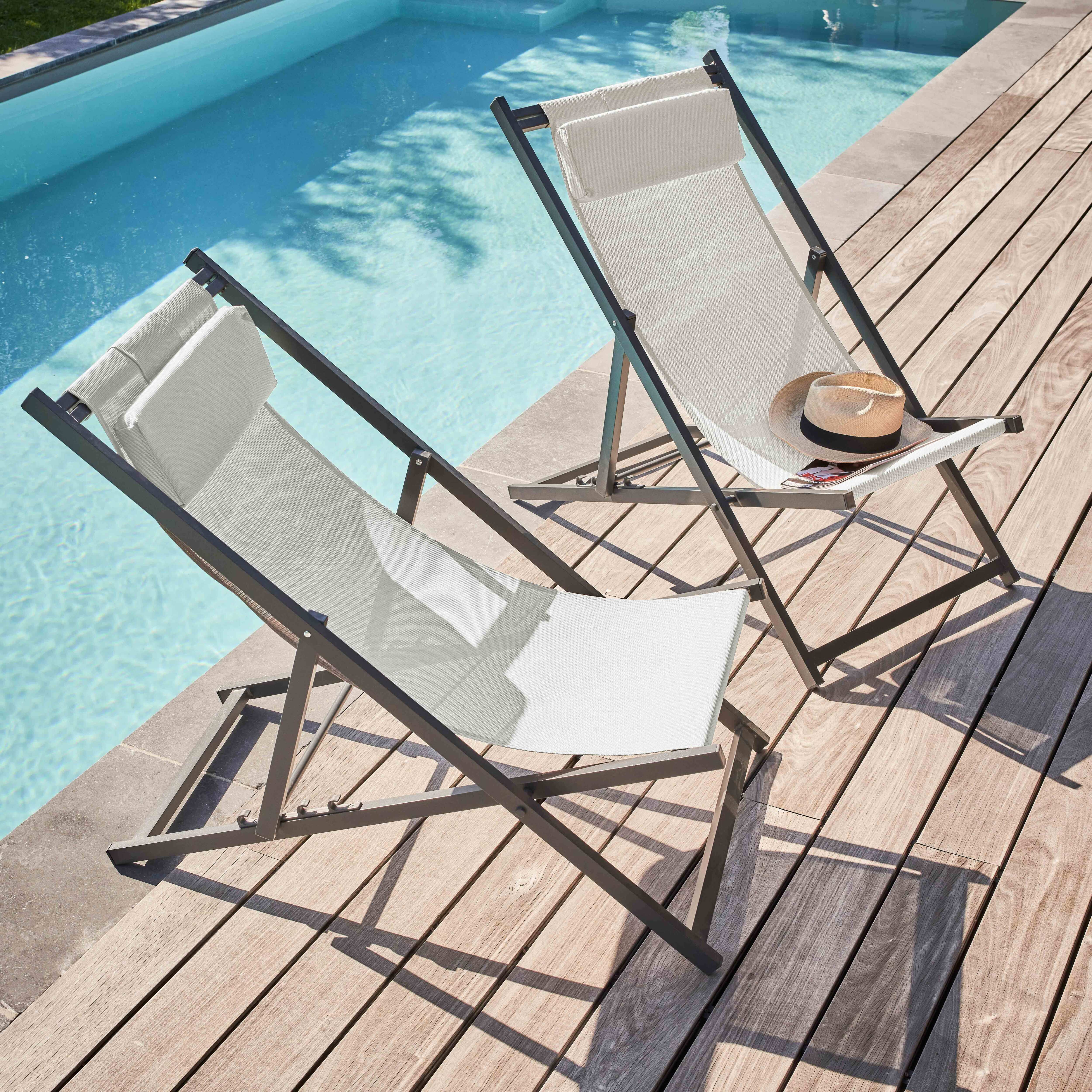 Zwei weiße Liegestühle auf Holzdeck neben einem Pool. Auf einem liegen ein Hut und ein Magazin. Blauer Pool im Hintergrund.