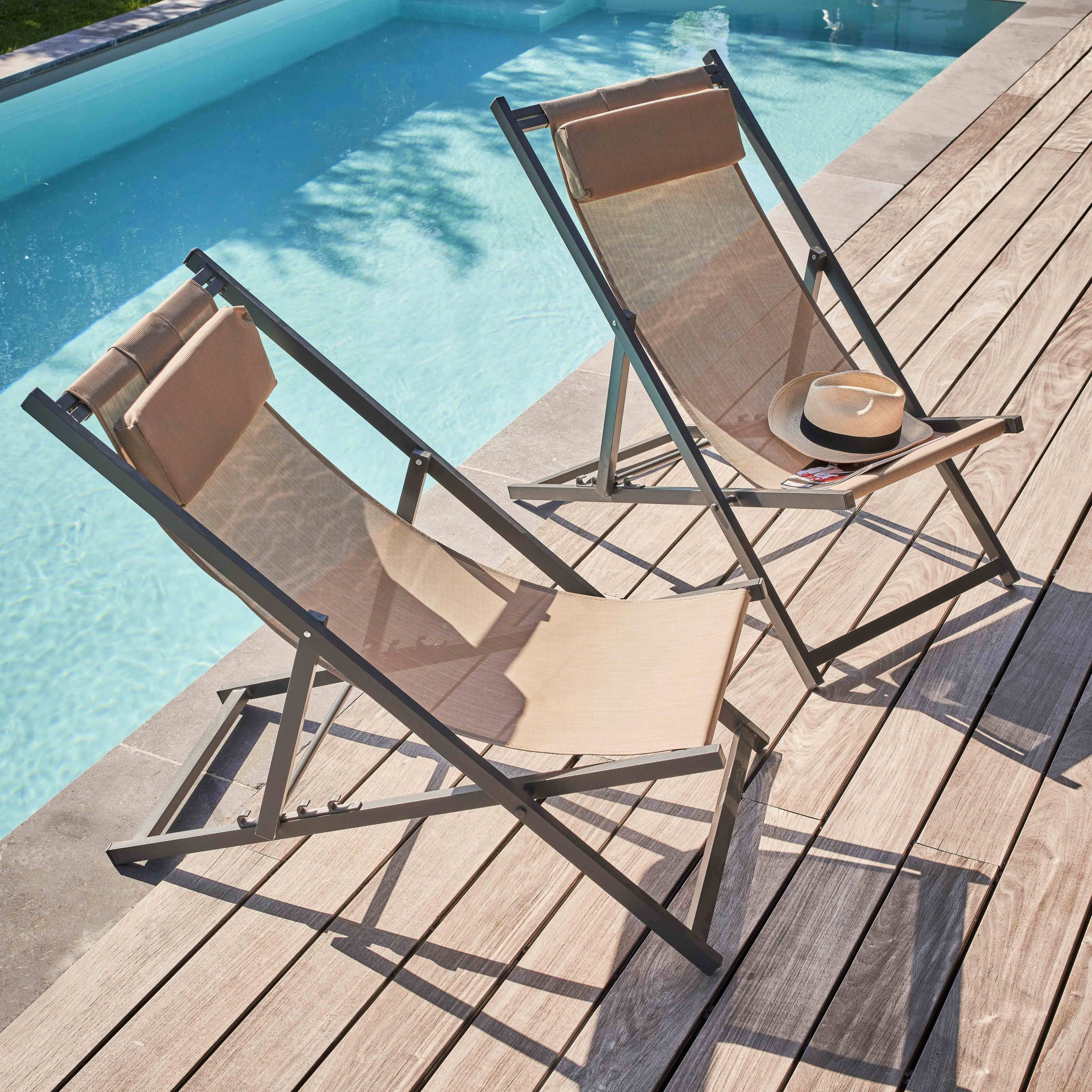 Zwei beige Liegestühle an einem Pool. Auf einem liegt ein Hut. Holzdeck umgibt den Pool.