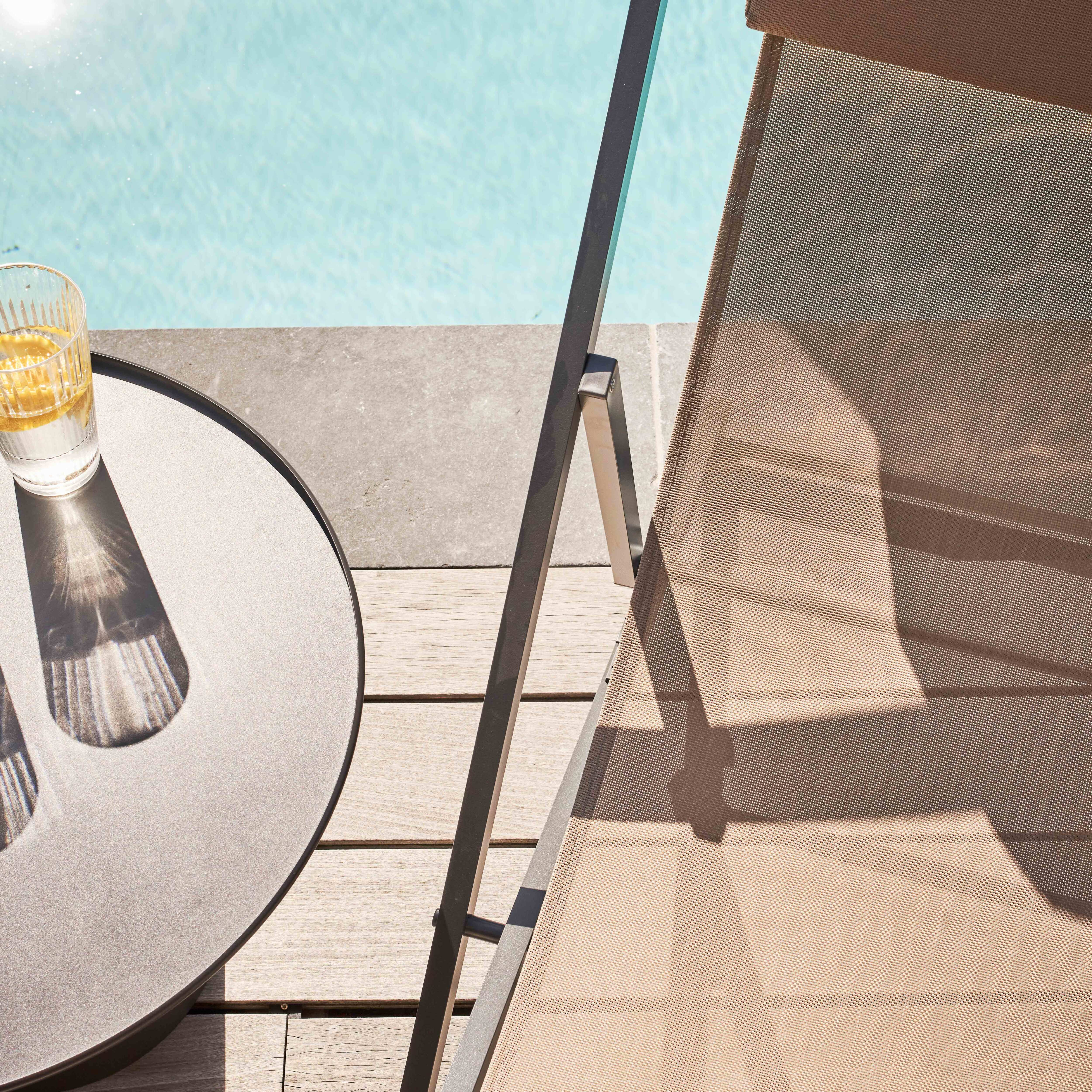 Glas mit Getränk, Tisch und Stuhl am Pool. Der Stuhl ist braun. Sonniger Tag.