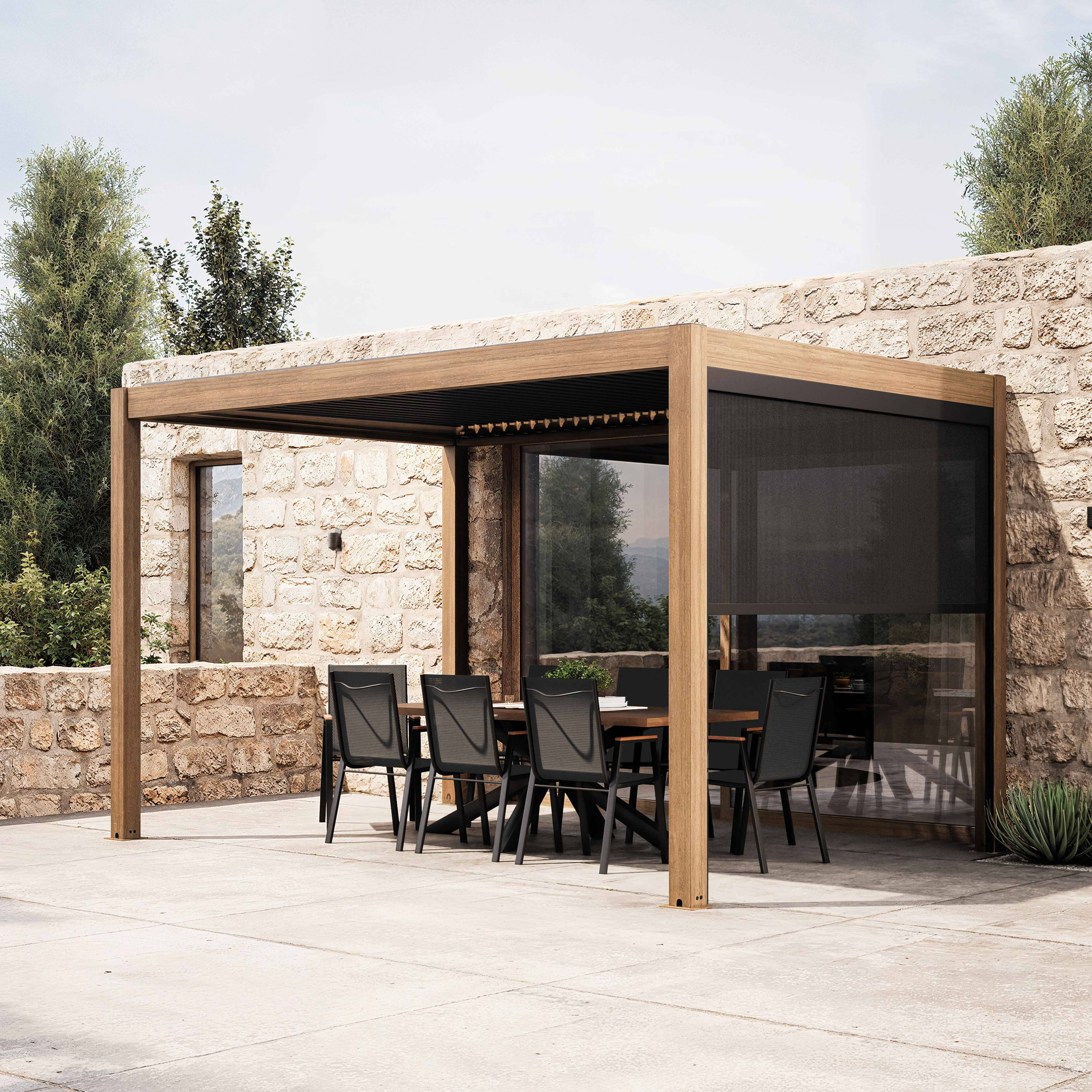 Essbereich im Freien mit Holzpergola, Tisch, Stühlen und Steinmauer im Hintergrund. Bäume und Himmel sichtbar.