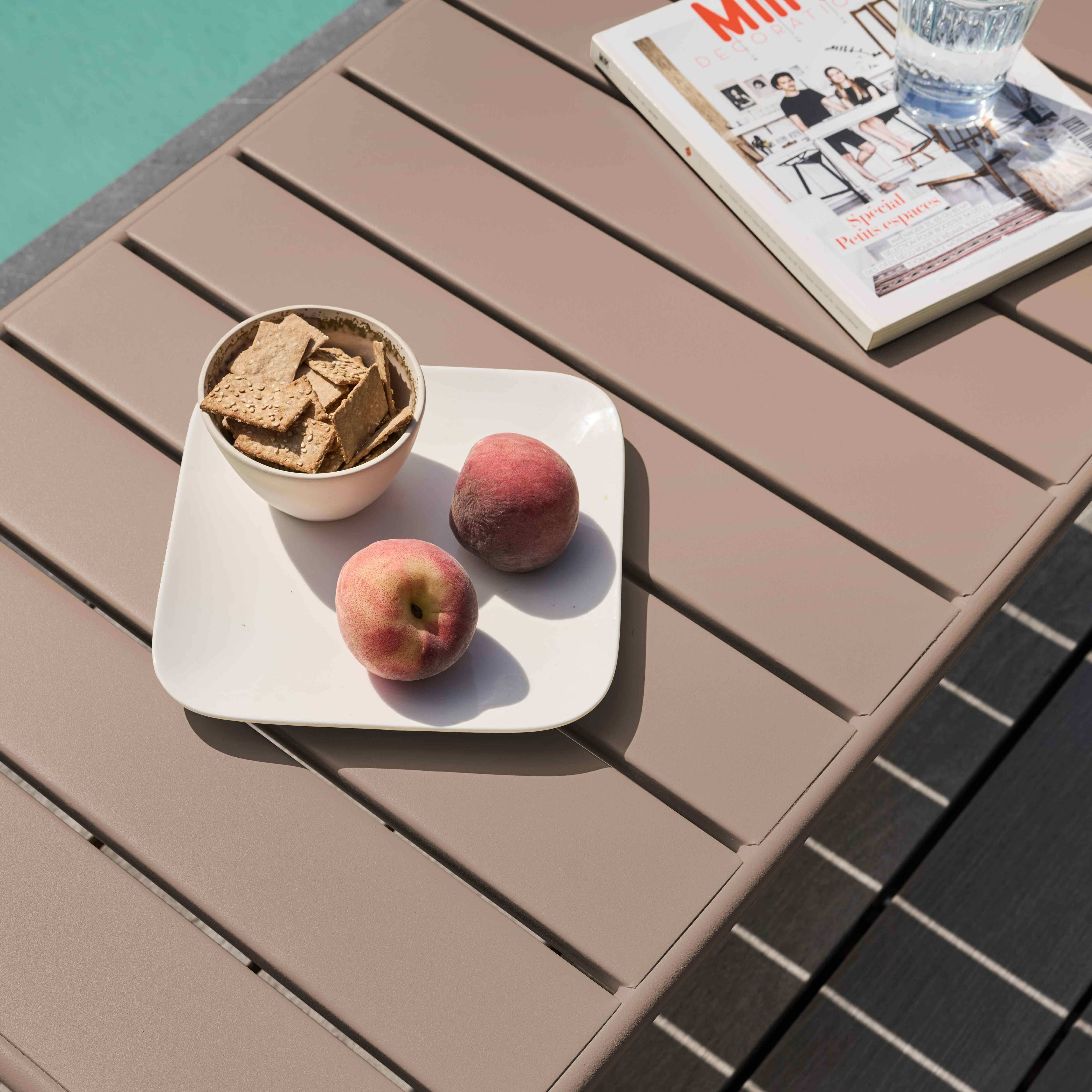 Ein Tisch mit Crackern, Pfirsichen und einer Zeitschrift. Ein Glas Wasser steht neben der Zeitschrift. Pool im Hintergrund.