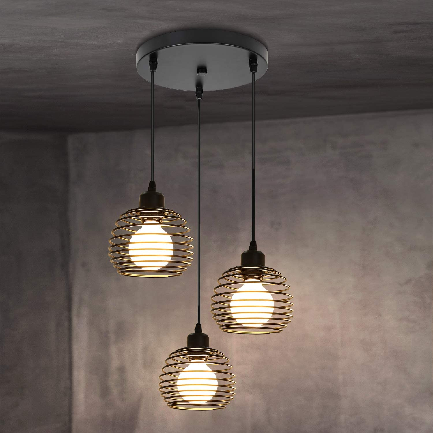 Trzy lampy wiszące zwisają z czarnej płyty sufitowej. Każda lampa ma klatkową, spiralną konstrukcję z jasną żarówką w środku.