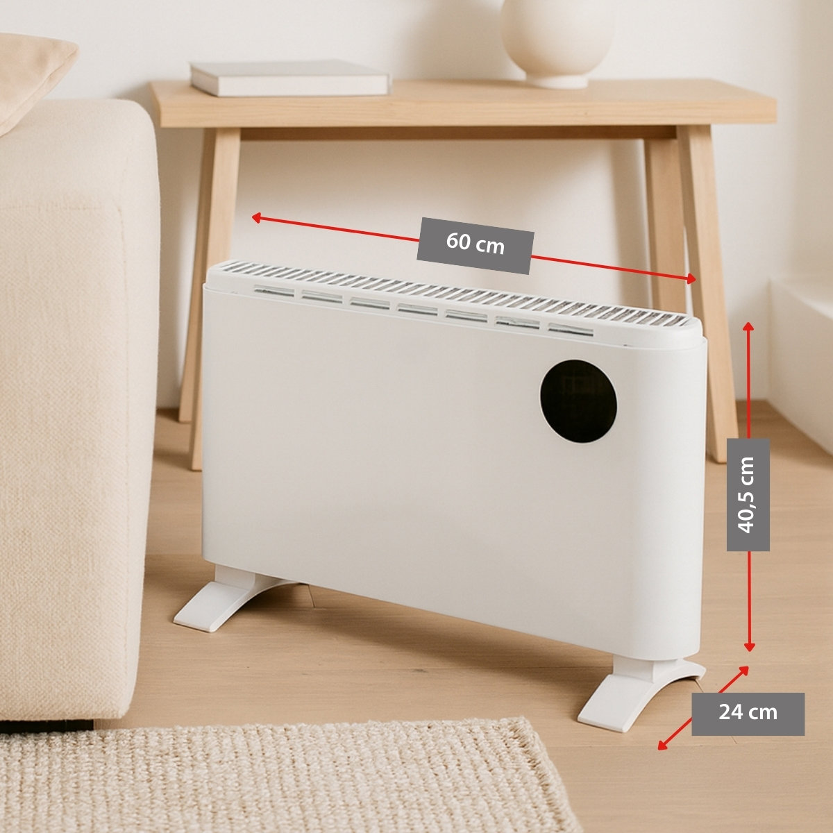Een witte elektrische kachel met afmetingen staat op de houten vloer. Een beige tapijt en bank staan op de voorgrond. Een tafel staat achter.