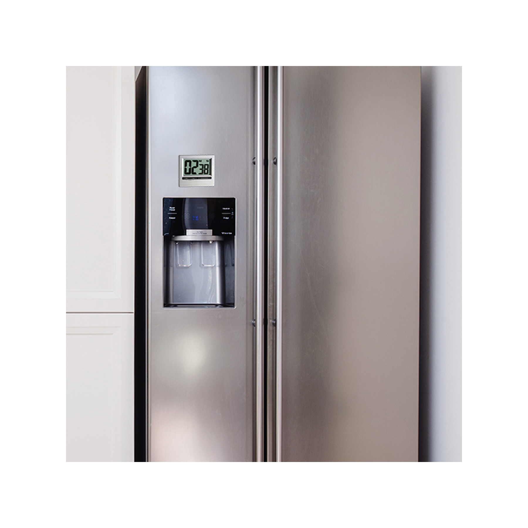 Ein Edelstahlkühlschrank mit Digitalanzeige, die 02:38 anzeigt. Weiße Schränke links.