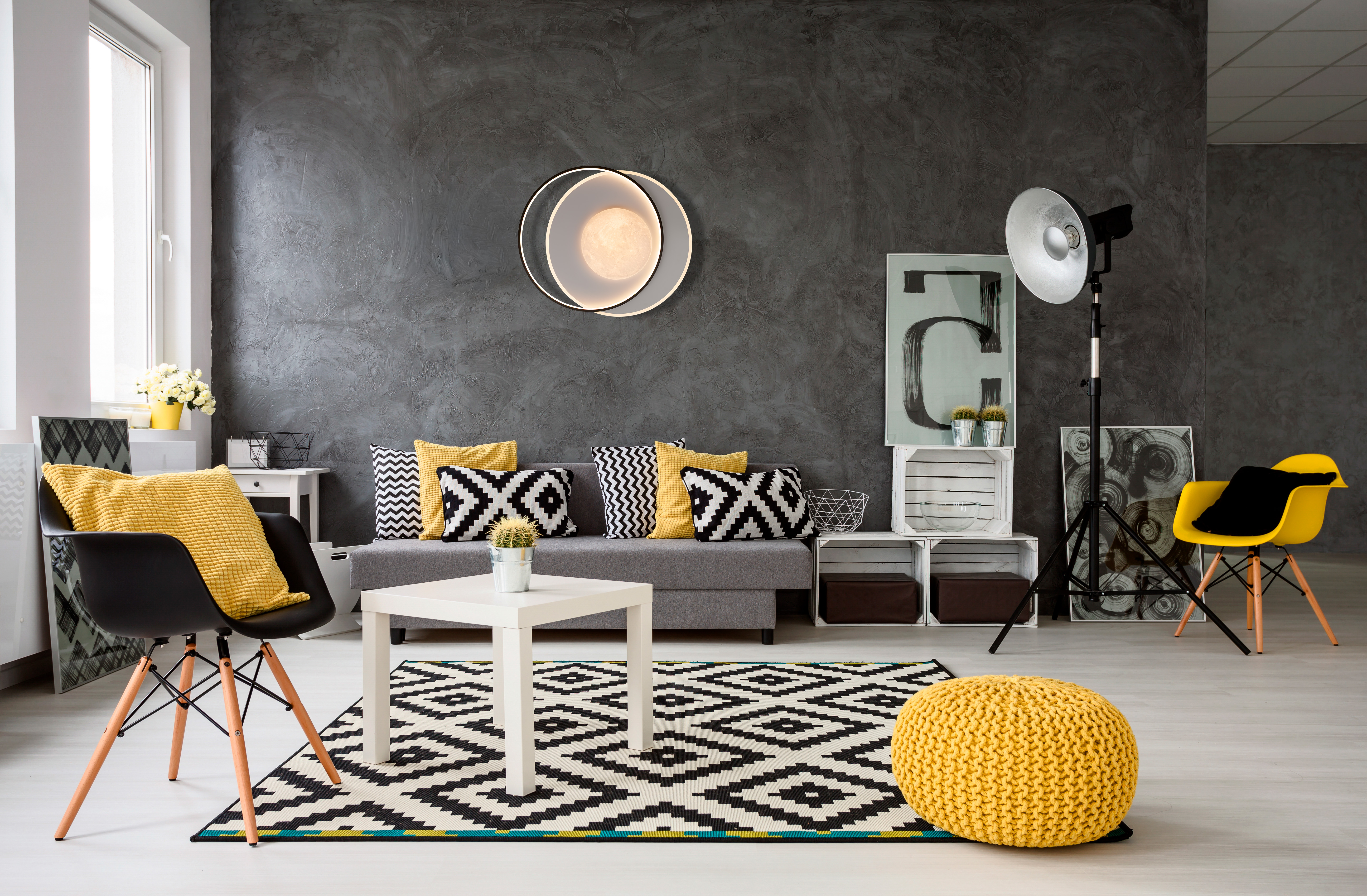 Ein modernes Wohnzimmer mit grauen Wänden, einem Sofa, einem Teppich, einem weißen Tisch, einem gelben Pouf und Stuhl.