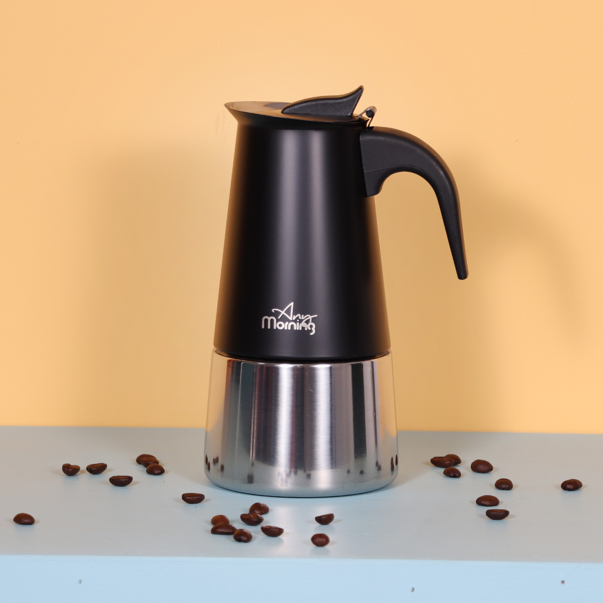 Mavi bir yüzeyde dağılmış kahve çekirdekleri ve sarı bir arka plan üzerinde siyah ve gümüş bir espresso makinesi.
