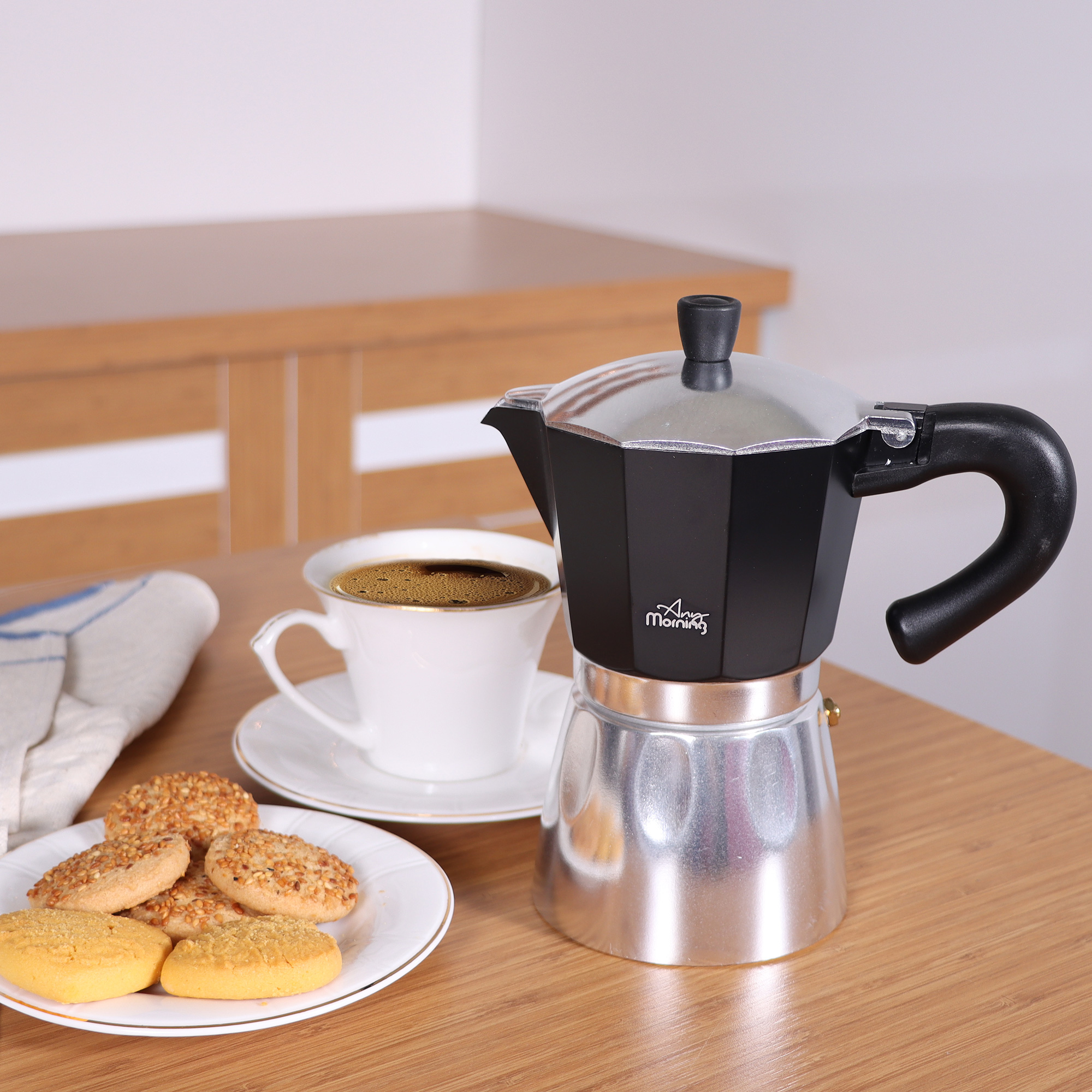 Siyah ve gümüş espresso makinesi, beyaz fincan, kurabiyeler ve ahşap bir masa ile bir kahve kurulumu.