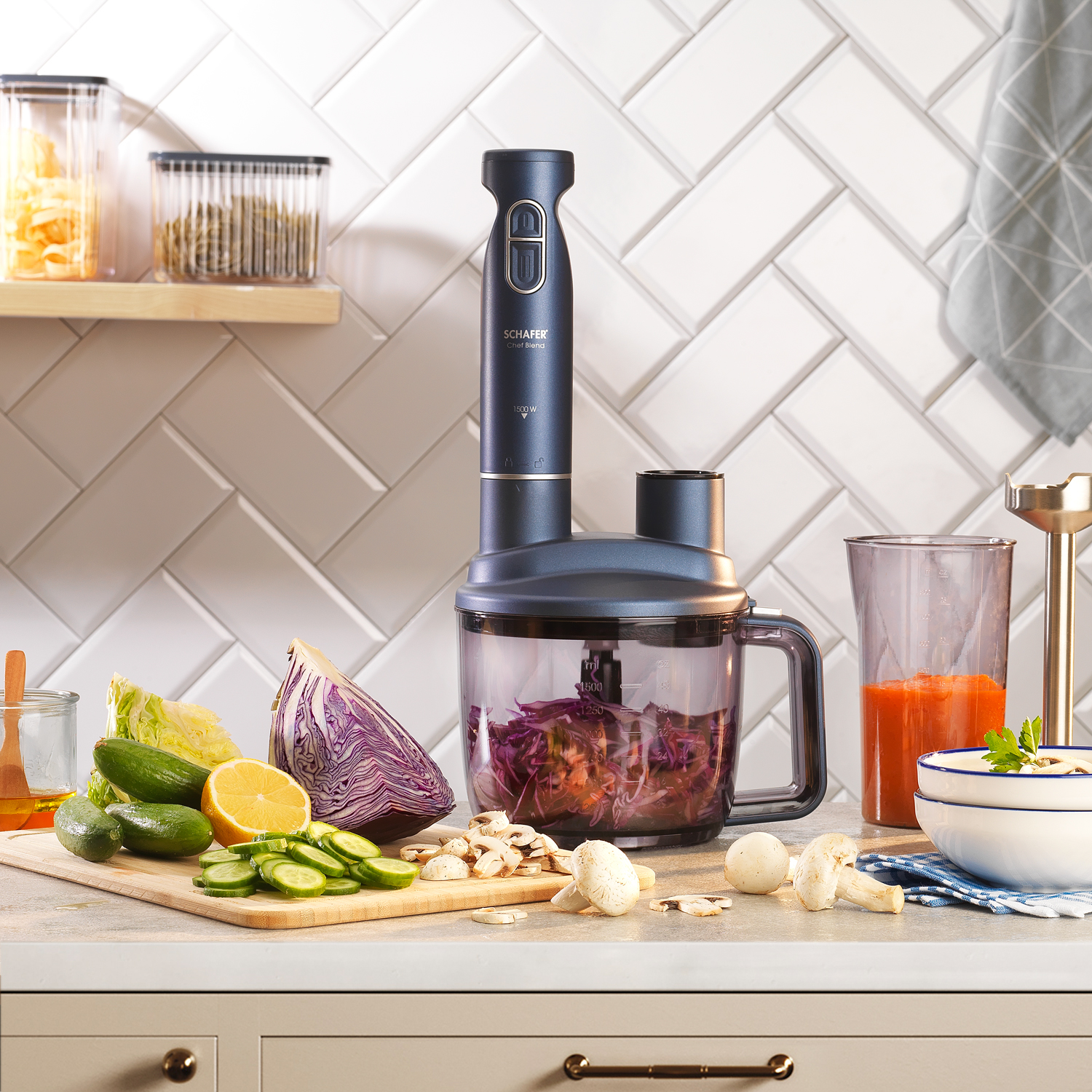 Bir mutfak sahnesi, bir blender, sebzeler ve hazırlanmış yiyecekler. Kesme tahtası, kase ve arka planda malzemelerle dolu kavanozlar içerir.