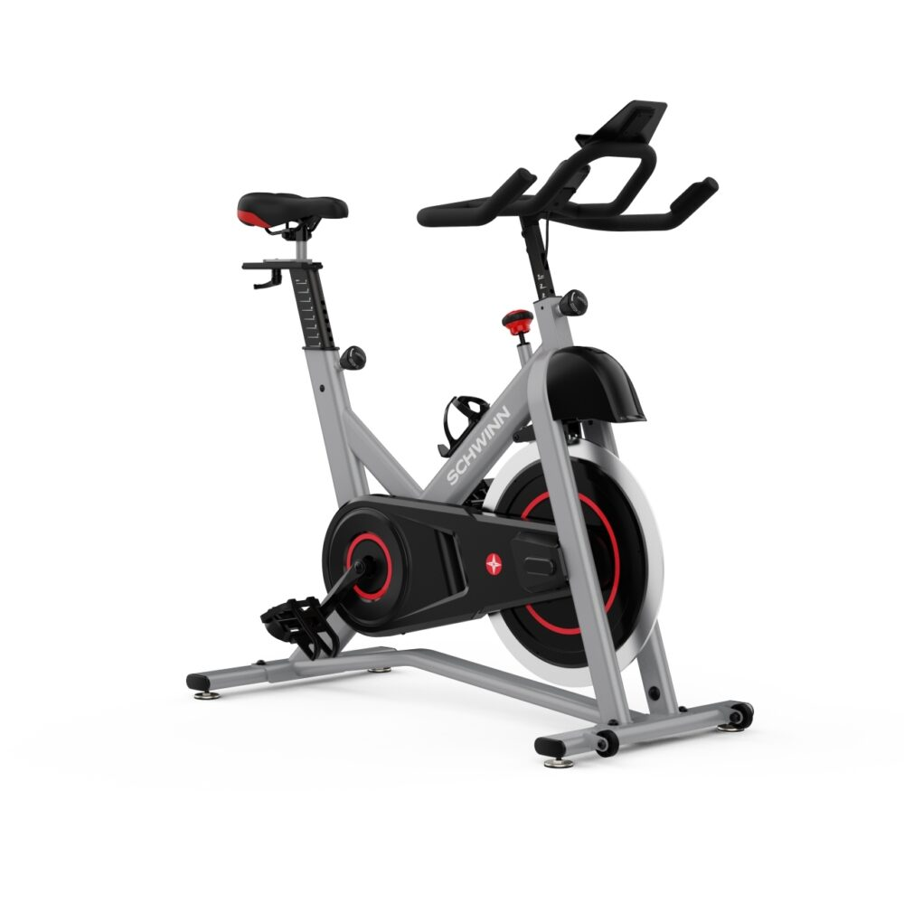 Un vélo d'exercice stationnaire gris avec des accents noirs et rouges. Il a une selle, un guidon et un porte-bouteille. La marque est Schwinn.