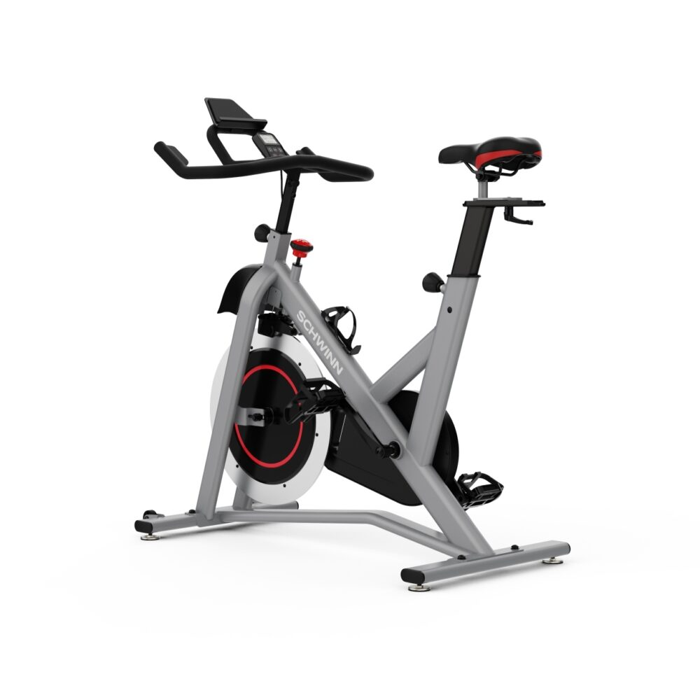 Un vélo d'exercice Schwinn gris. Il a une selle noire avec des touches de rouge, un guidon noir et un volant d'inertie bordé de rouge.
