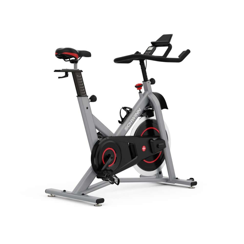 Un vélo d'exercice Schwinn stationnaire. Cadre gris avec des accents noirs et rouges. Il a une selle, un guidon et un écran.