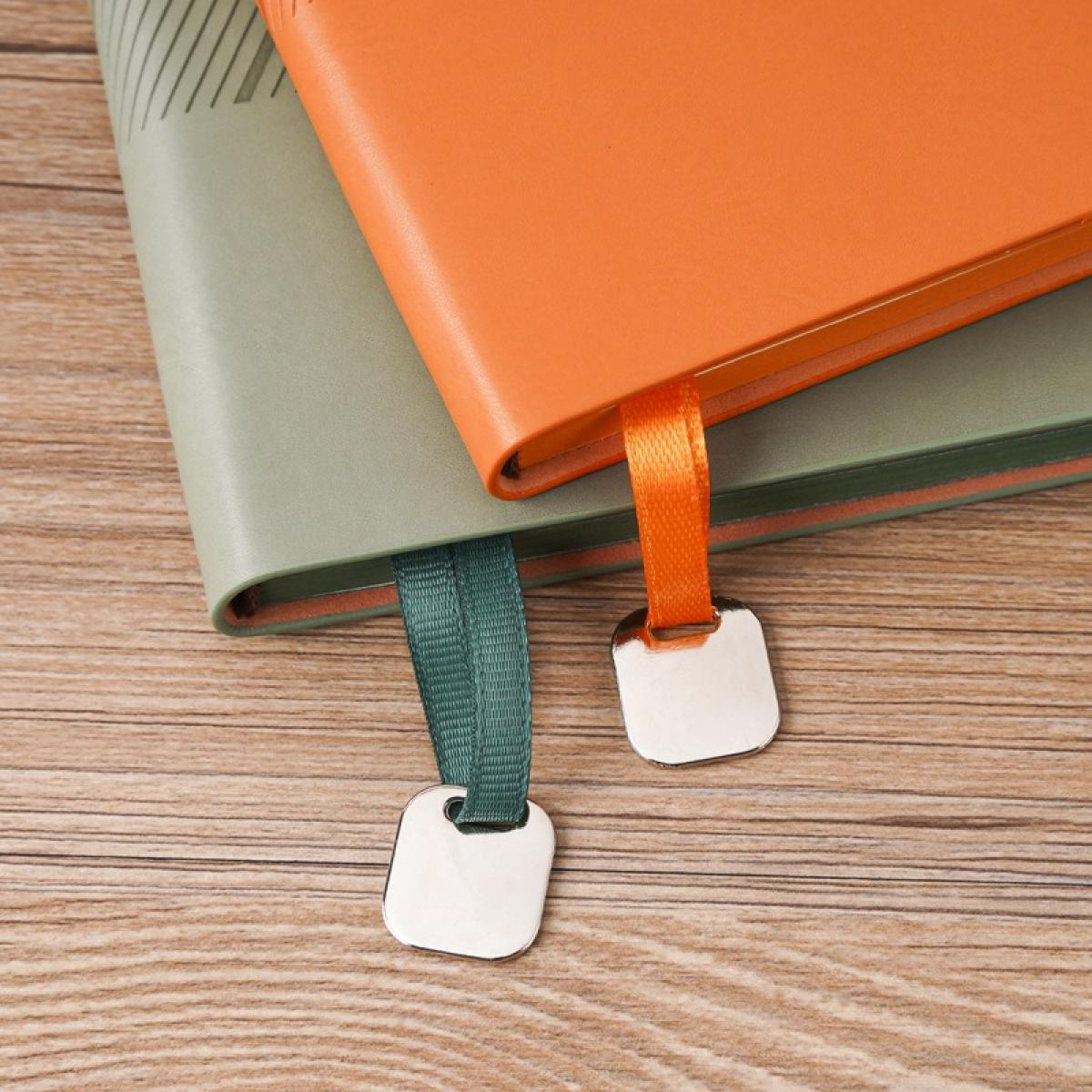 Zwei Notizbücher, eines orangefarben, eines grün, mit Bändchen und silbernen Anhängern, auf Holzoberfläche.