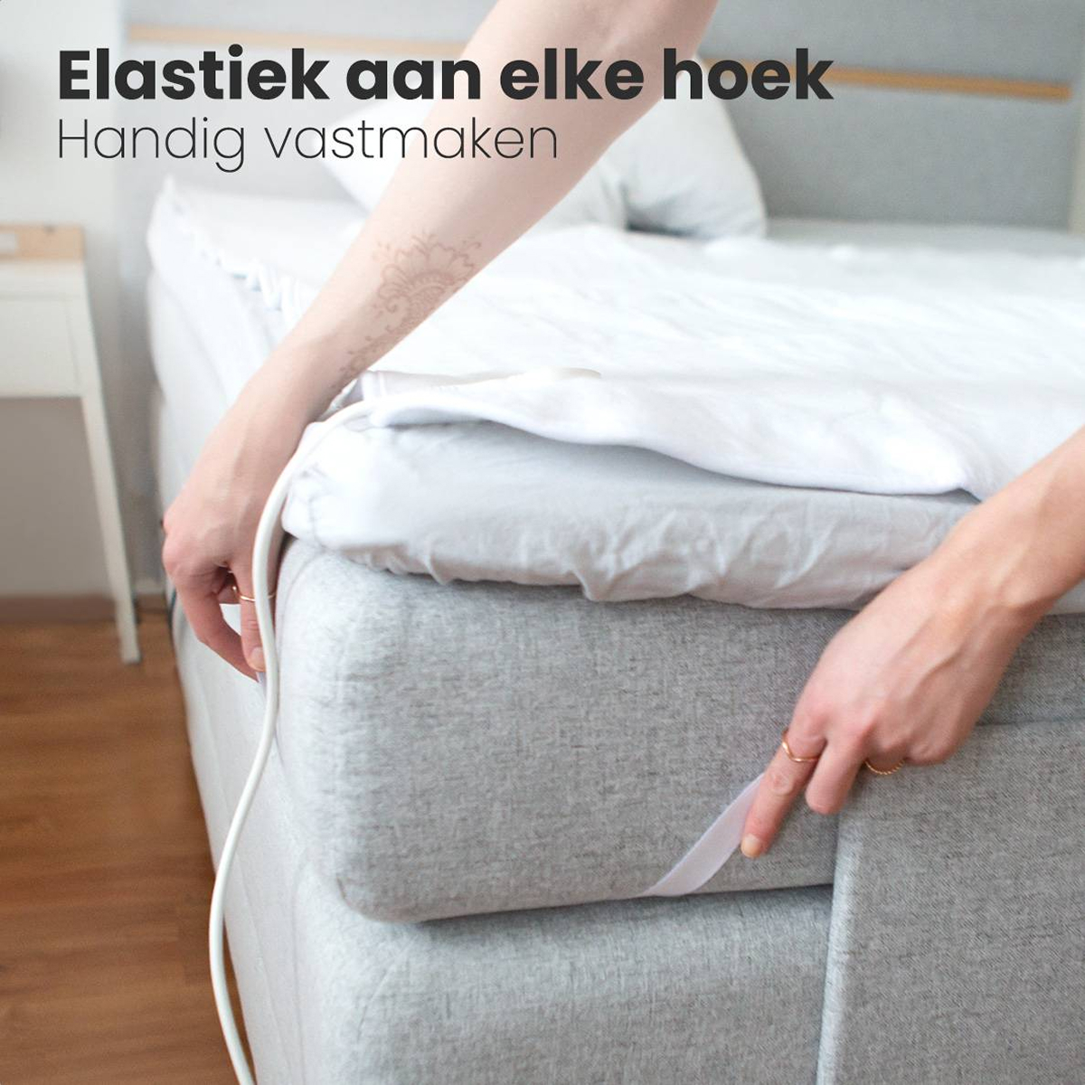 Mains fixant un drap blanc à un matelas gris. Le texte indique un élastique à chaque coin pour une fixation facile.