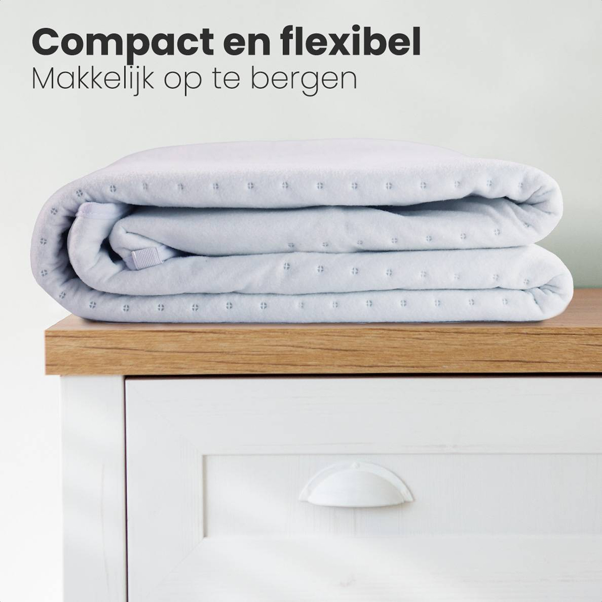 Une couverture bleu clair pliée repose sur une surface en bois au-dessus d'une armoire blanche. Le texte en haut indique 'Compact en flexibel.'