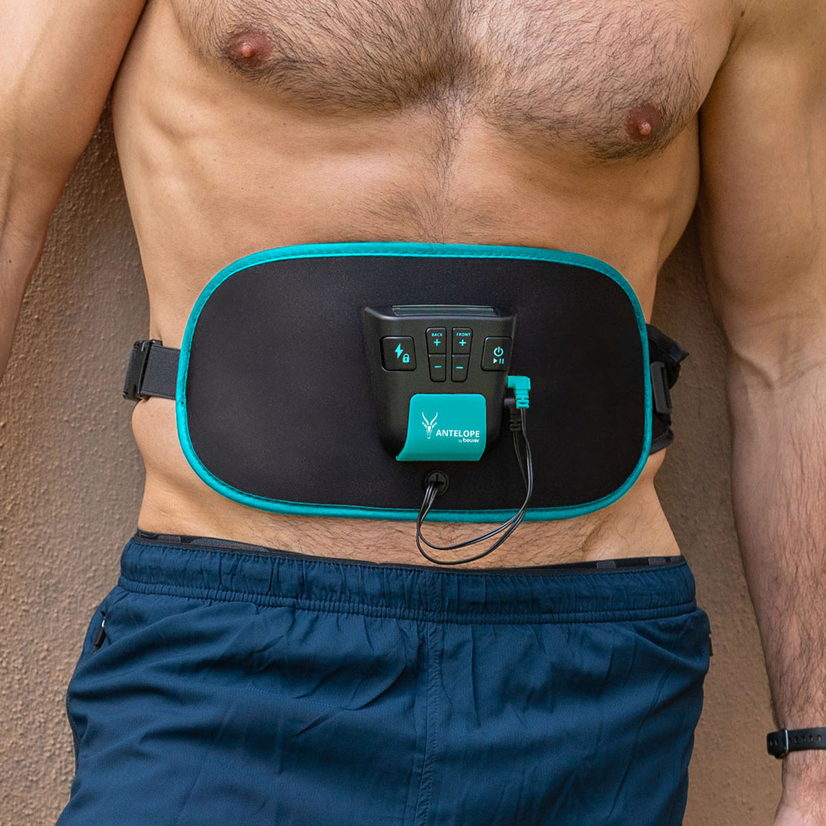 Ein Mann mit einem Fitnessgerät am Bauch. Das Gerät ist schwarz und türkis. Er trägt blaue Shorts und hat eine Uhr am Handgelenk.