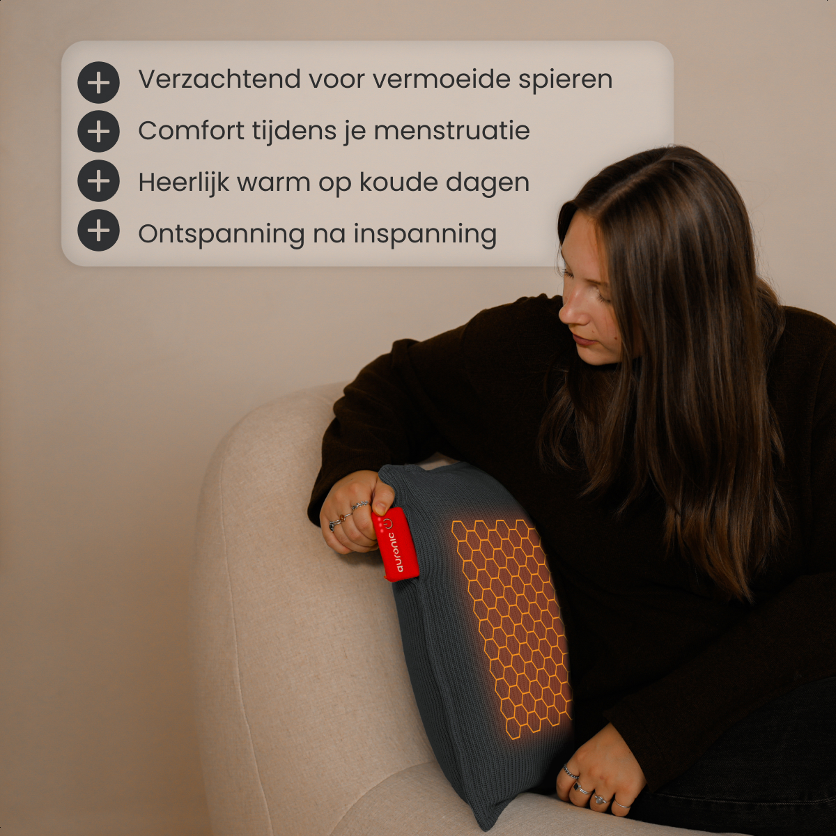 Een vrouw zit met een grijze warmtepad. De pad heeft een rood label. De tekst hierboven geeft voordelen. Ze zit in een neutrale kamer.