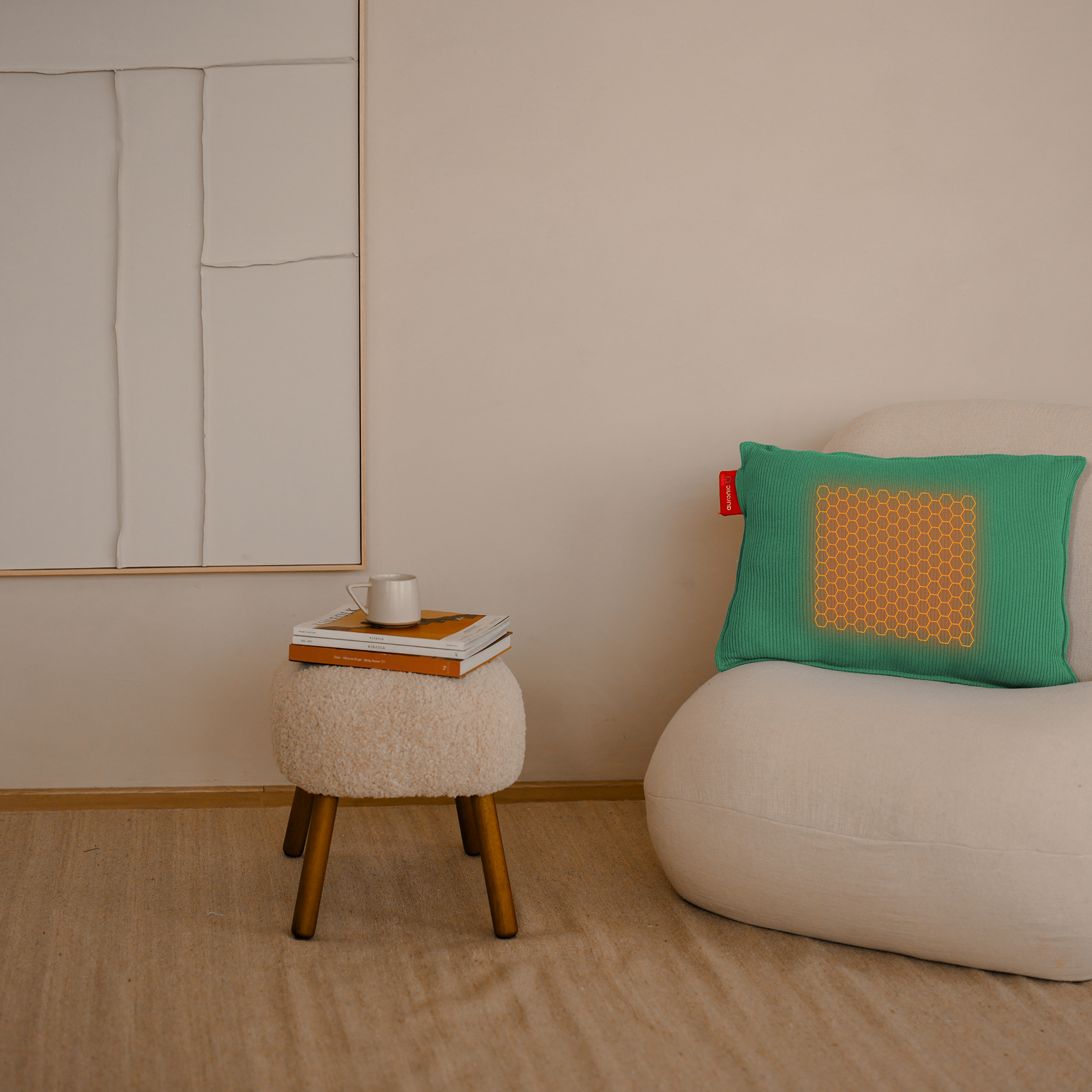 Une pièce avec une chaise blanche, un tabouret avec des livres et une tasse, et un oreiller vert avec un motif jaune.
