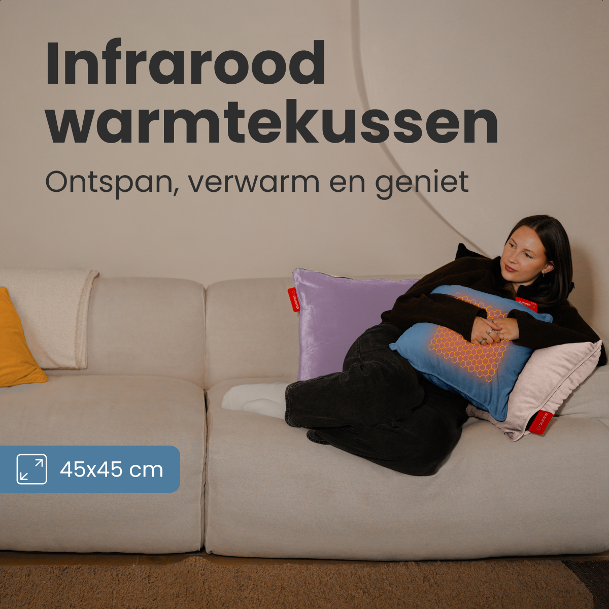 Une femme sur un canapé beige tient un coussin chauffant bleu. Des oreillers de différentes couleurs sont sur le canapé. Texte : 'Infrared warmtekussen'.