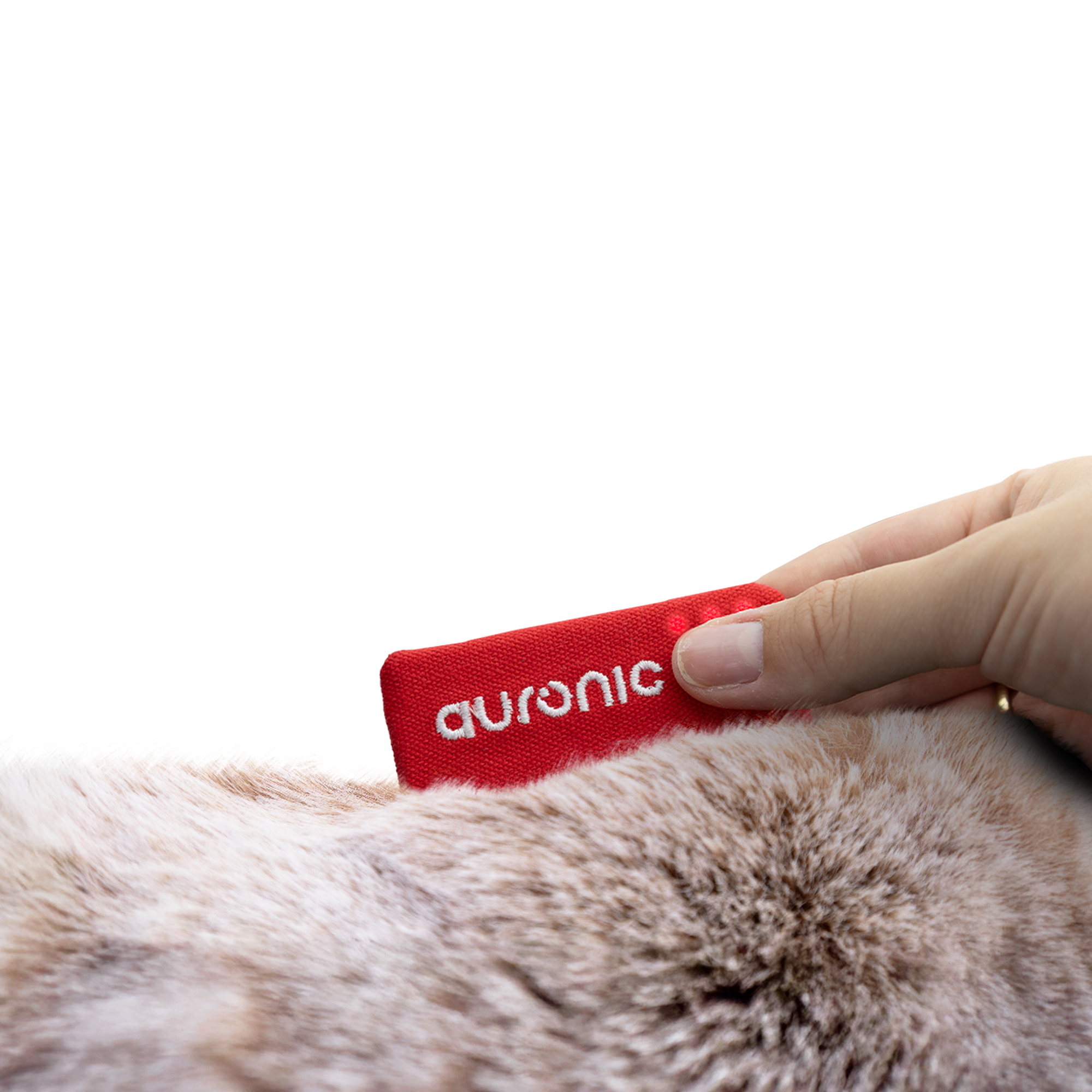 Une main tient un objet rectangulaire rouge étiqueté 'auronic' sur une fourrure animale brun clair, sur fond blanc.