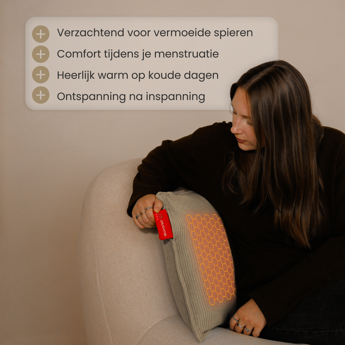 Een vrouw zit op een beige stoel en houdt een grijs kussen vast met een rood label. Het kussen heeft een oranje patroon.