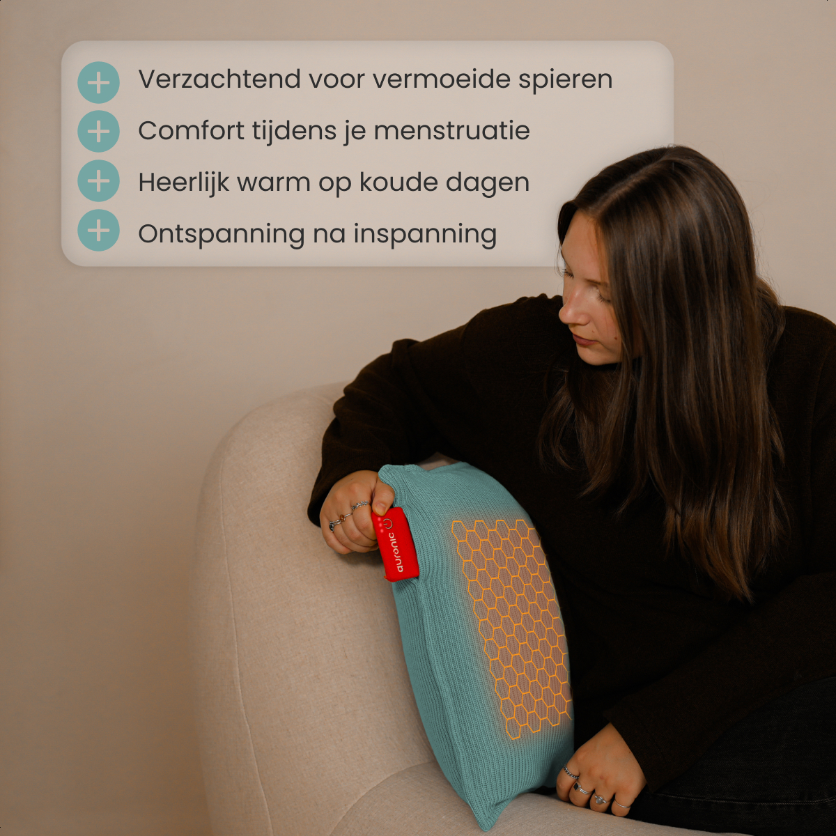 Een vrouw houdt een turquoise warmtekussen vast op een beige stoel. Het kussen heeft een oranje honingraatpatroon. De tekst op het kussen luidt 'auronic'.