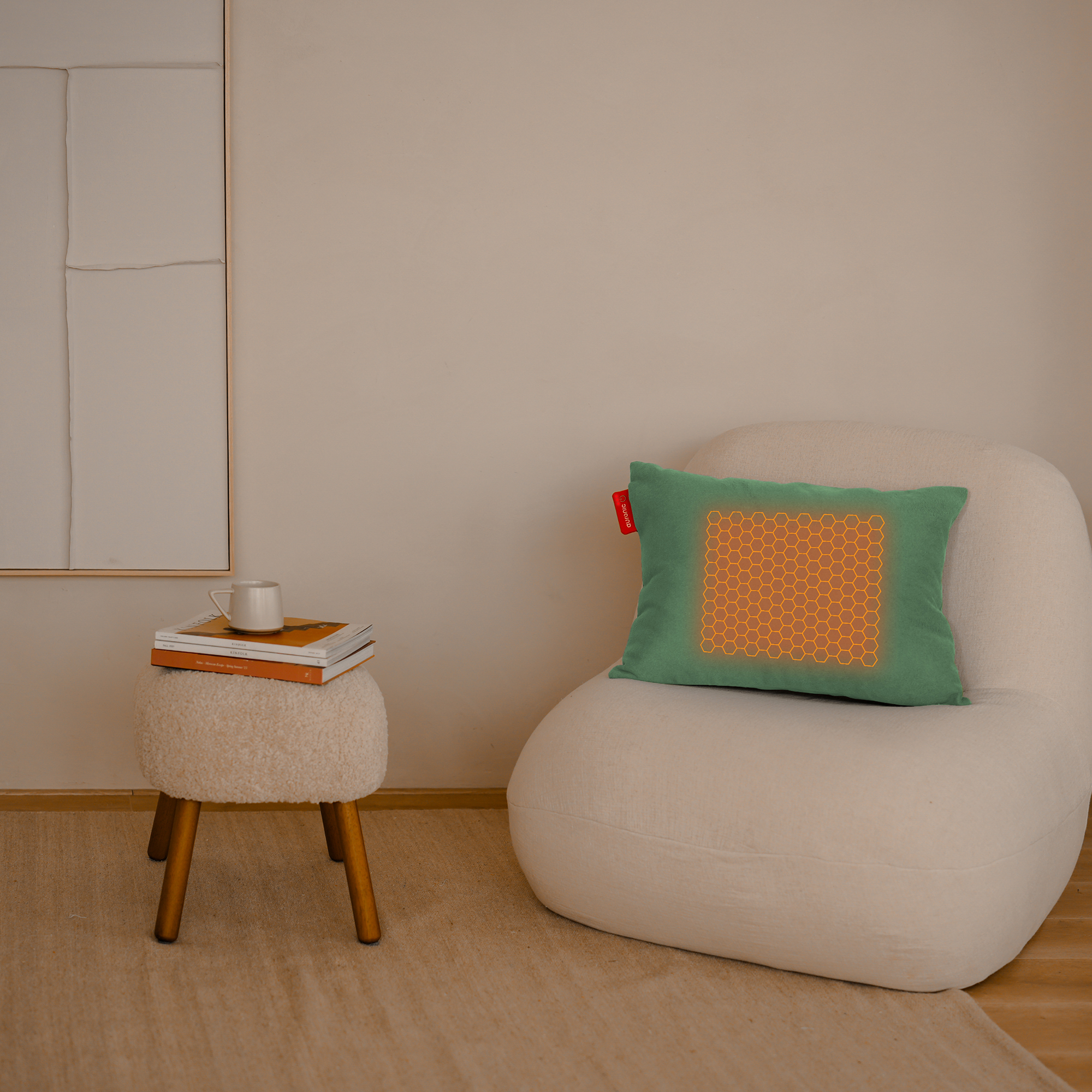 A green pillow with a honeycomb design on a white chair. A small table with books and a cup. Beige background.