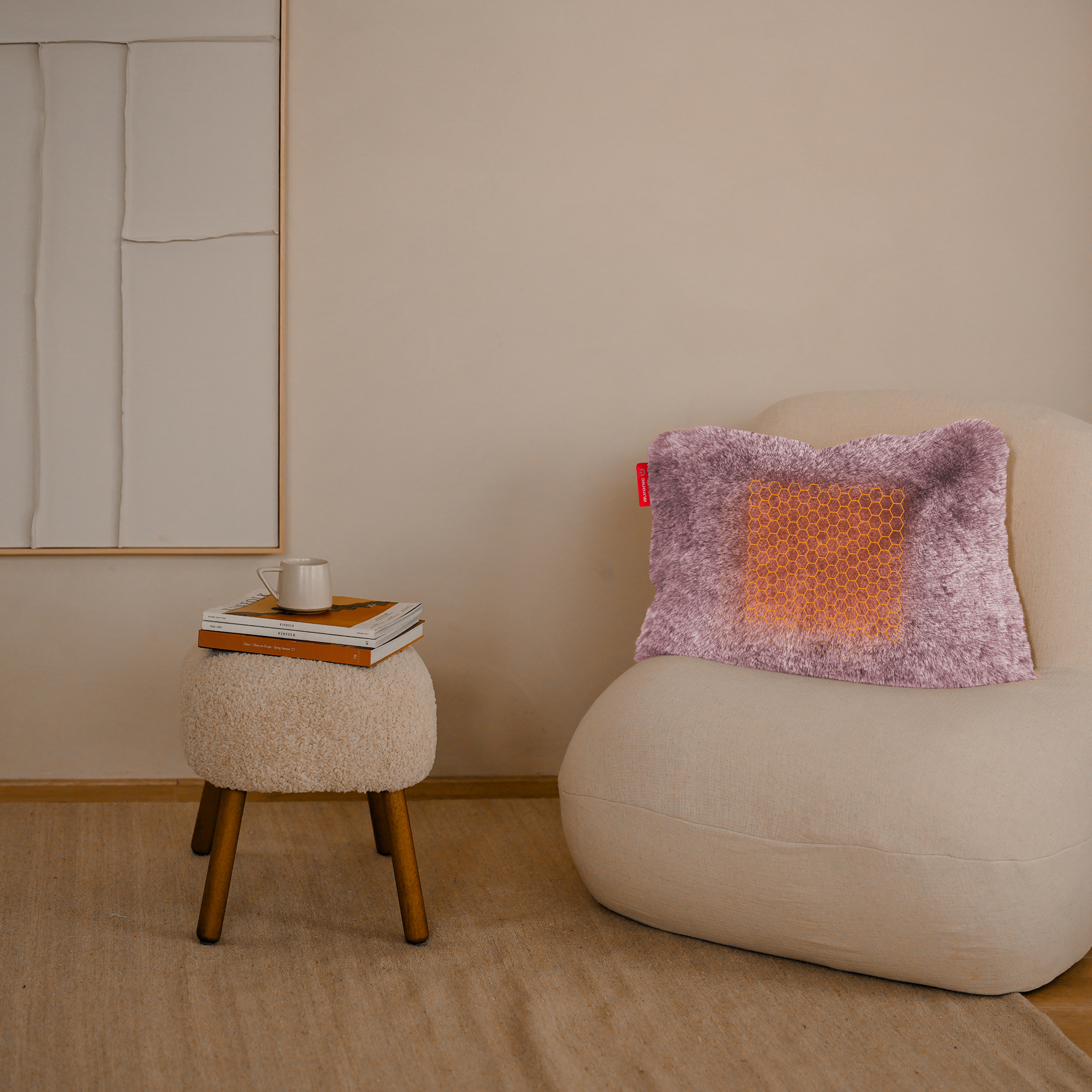 Een kamer met een crèmekleurige stoel en een kruk met boeken en een mok. Er ligt een kussen op de stoel.