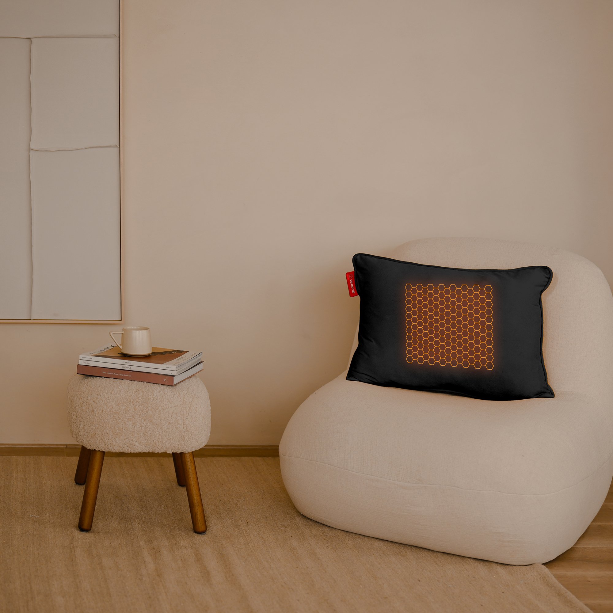 Een kamer met een witte stoel en kruk. Op de stoel ligt een zwart kussen met een oranje honingraatpatroon. Een kopje en boeken staan op de kruk.
