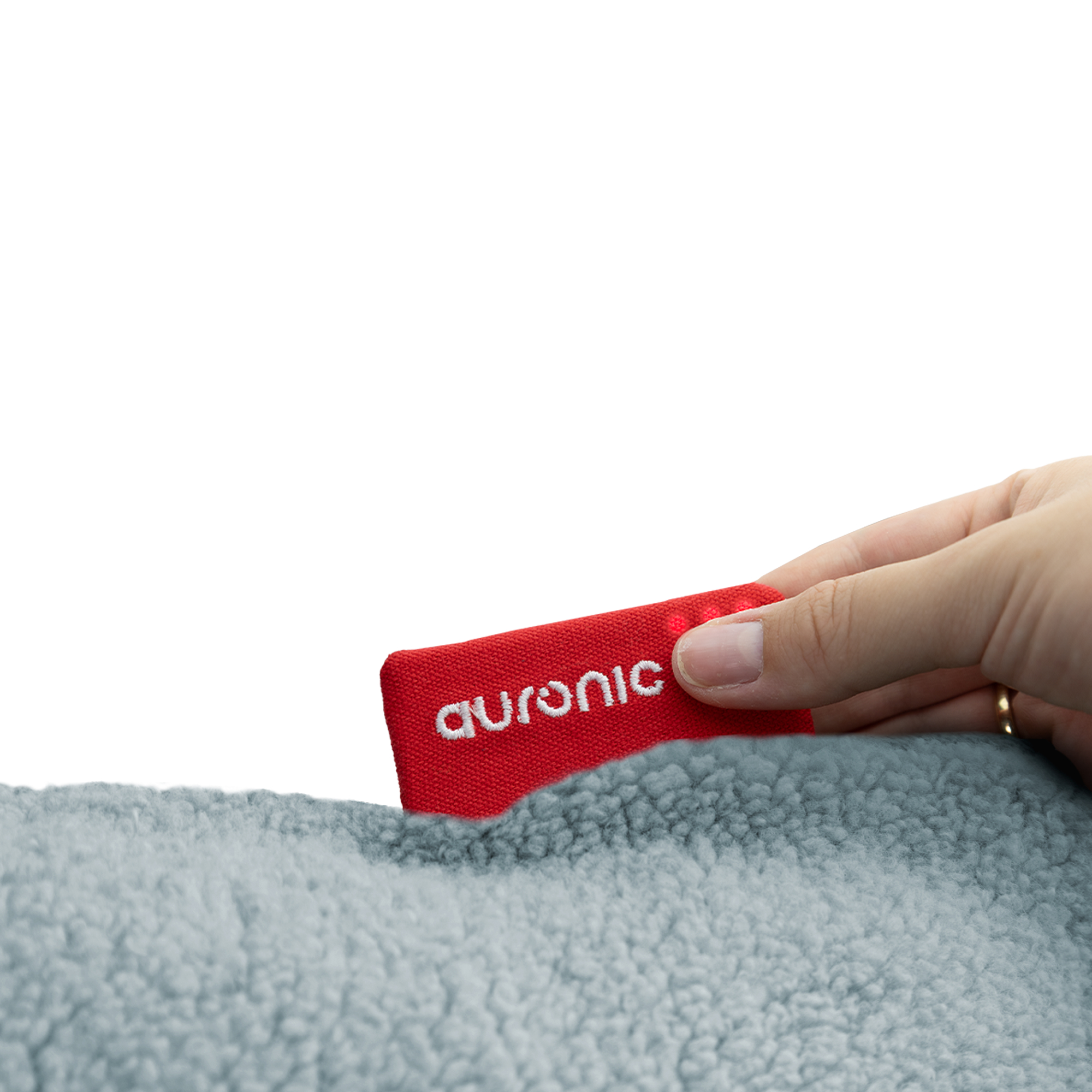 A hand holds a red tag with 'auronic' on it over gray, fluffy fabric. White background.