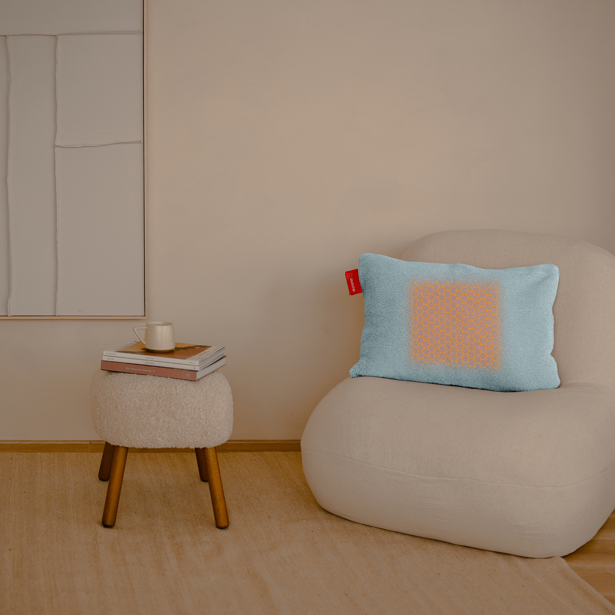 A room with a chair and a small table. A pillow with an orange pattern sits on the chair. A cup and books on the table.