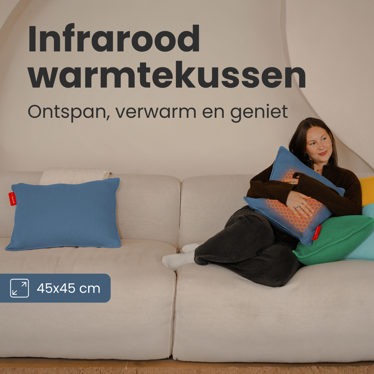 Femme sur un canapé tenant un oreiller infrarouge bleu. Un oreiller bleu et d'autres coussins colorés sont à côté d'elle. Texte : 'Infrarood warmtekussen'.