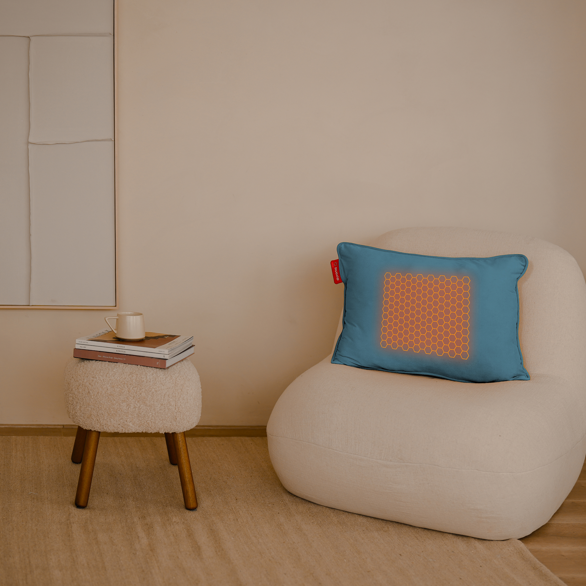 Un oreiller bleu avec un motif en nid d'abeilles orange repose sur une chaise blanche. Un petit tabouret contient des livres et une tasse.